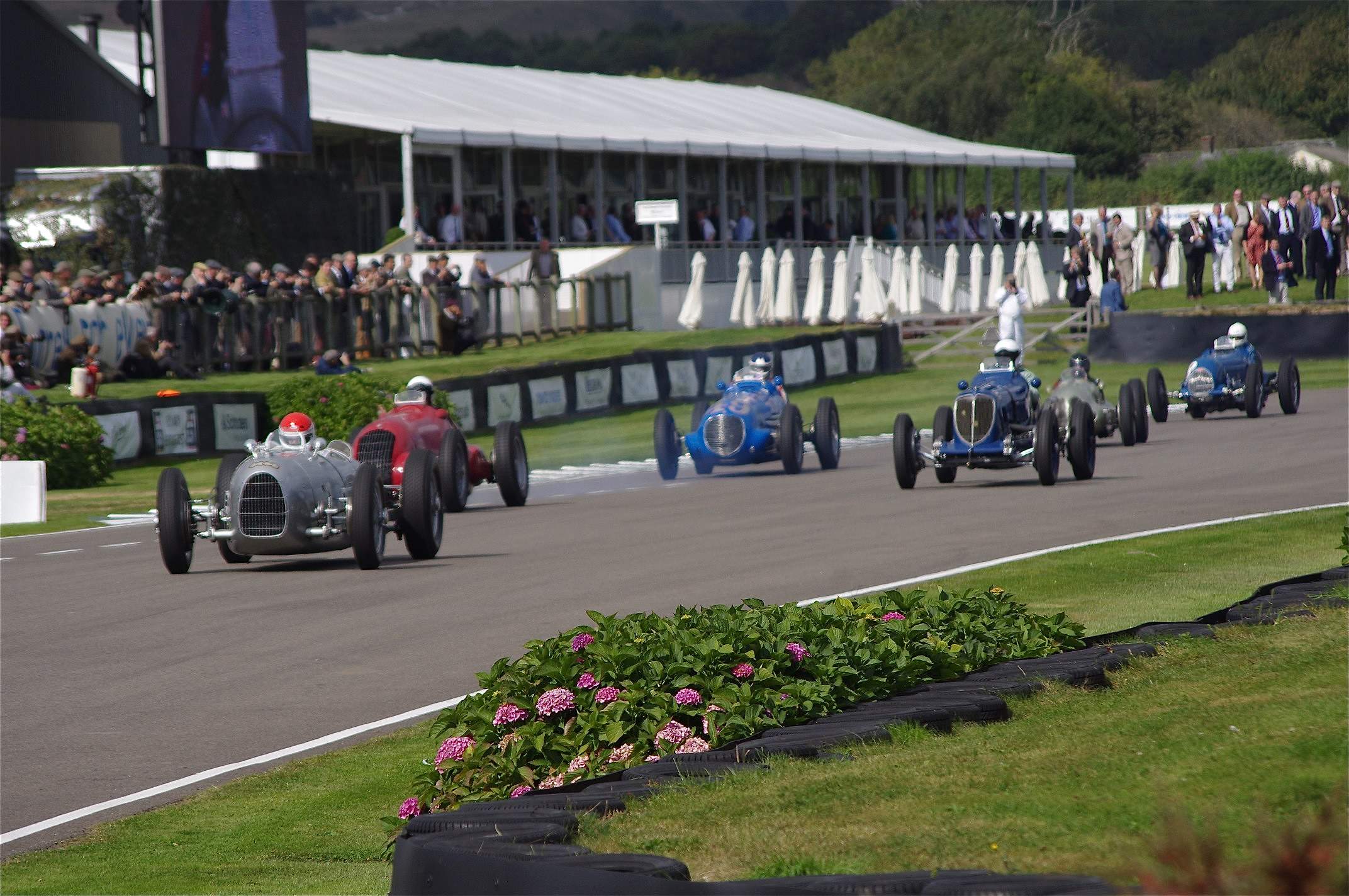 Pre-war Grand Prix cars racing on the Goodwood Motor Circuit at the Revival with a period crowd behind