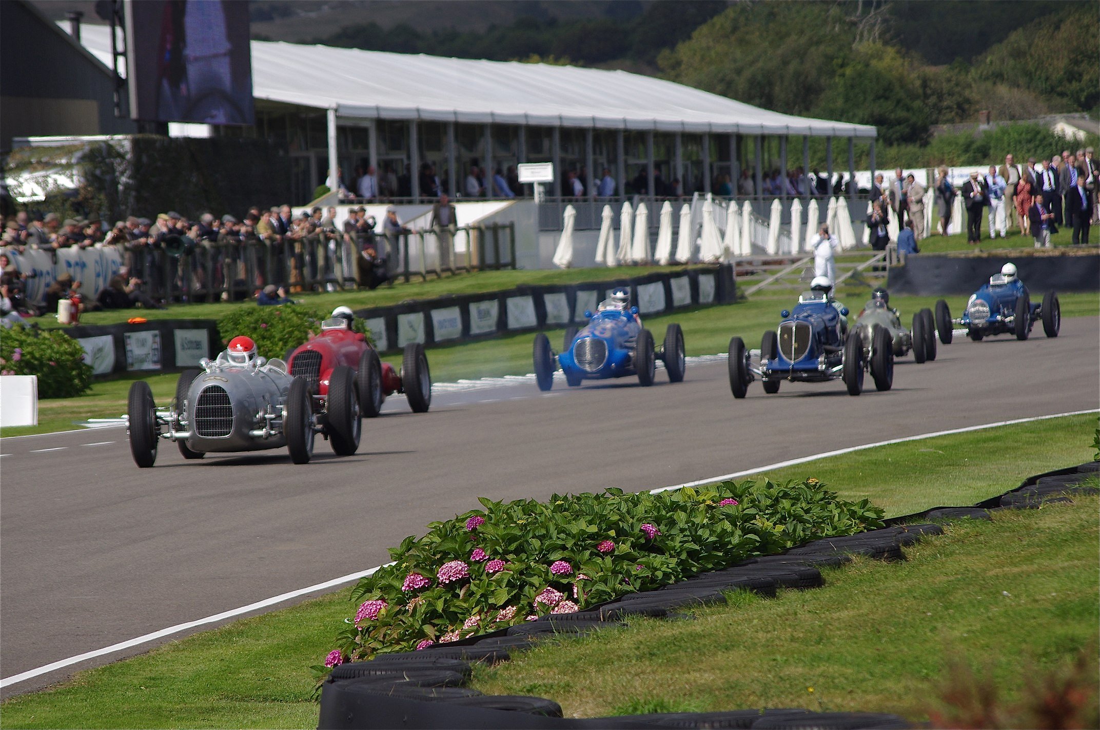 Pre-war Grand Prix cars racing on the Goodwood Motor Circuit at the Revival with a period crowd behind