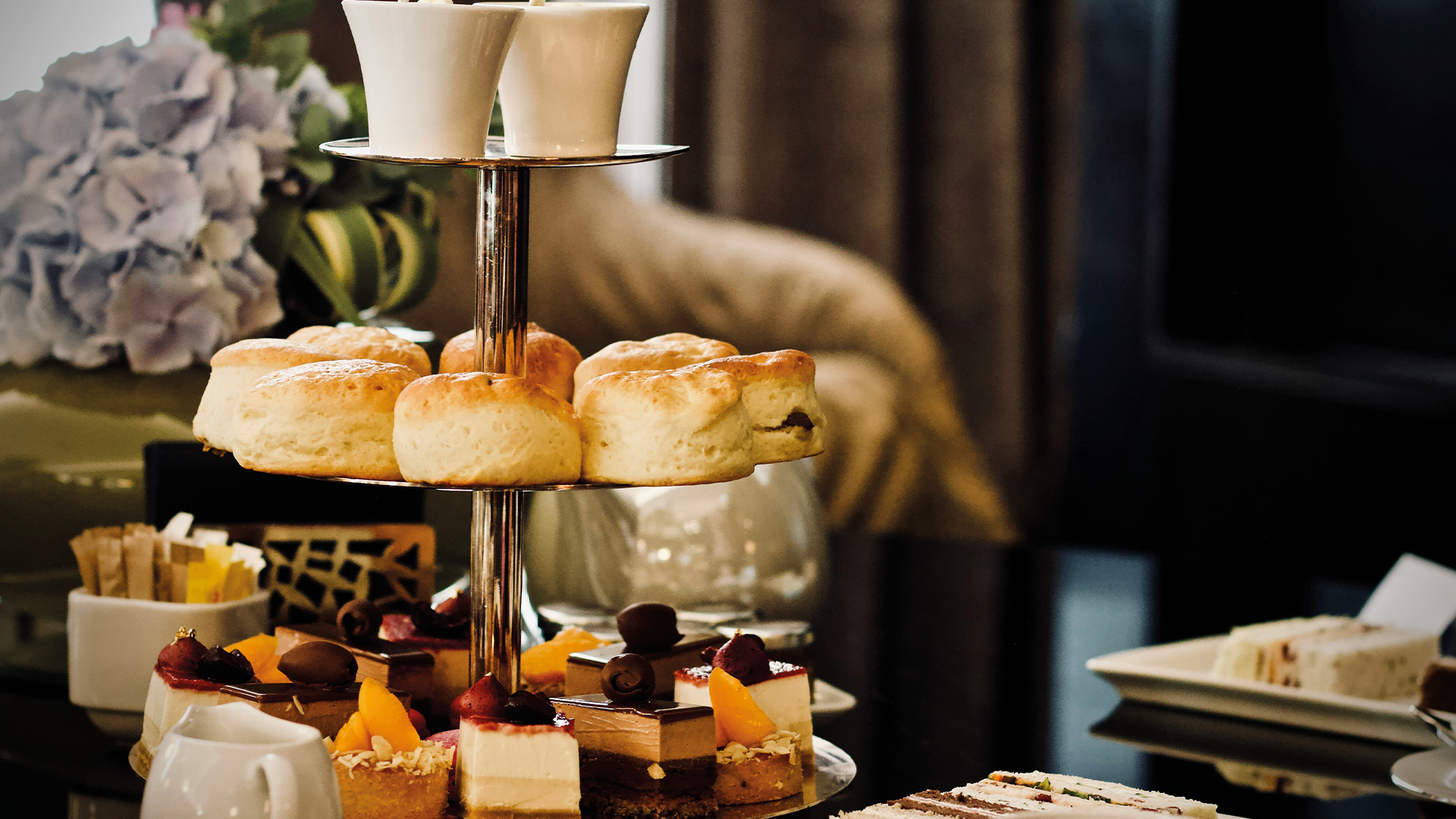 Elegant afternoon tea service with tiered cake stand, pastries and cream on white tablecloth