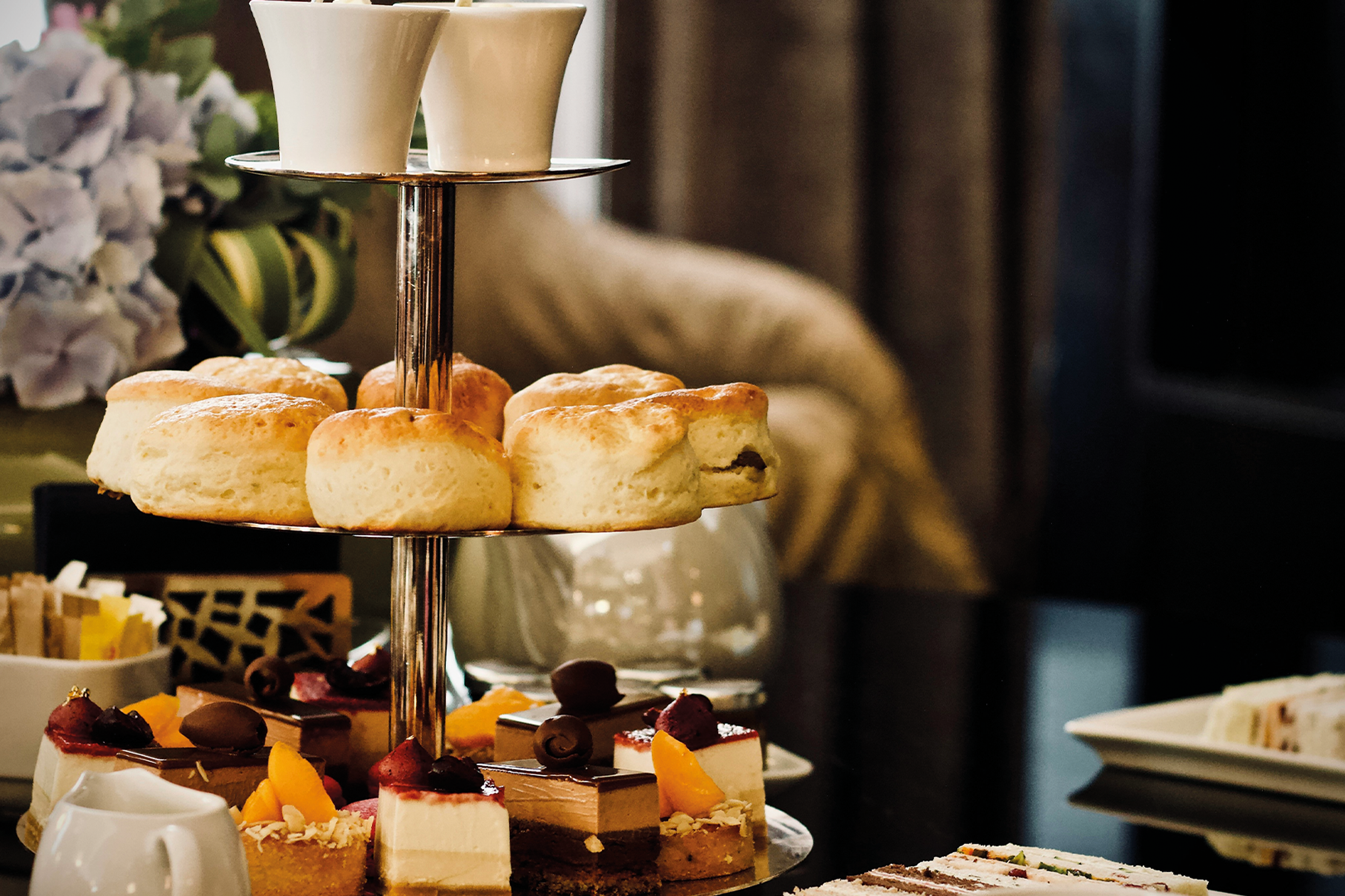 Elegant afternoon tea service with tiered cake stand, pastries and cream on white tablecloth