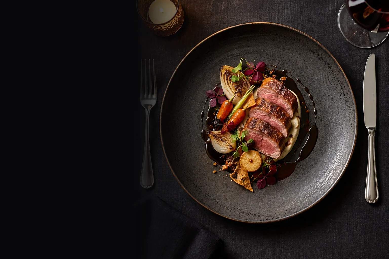 A plated course of sliced duck, glazed vegetables and jus on a dark stoneware plate.