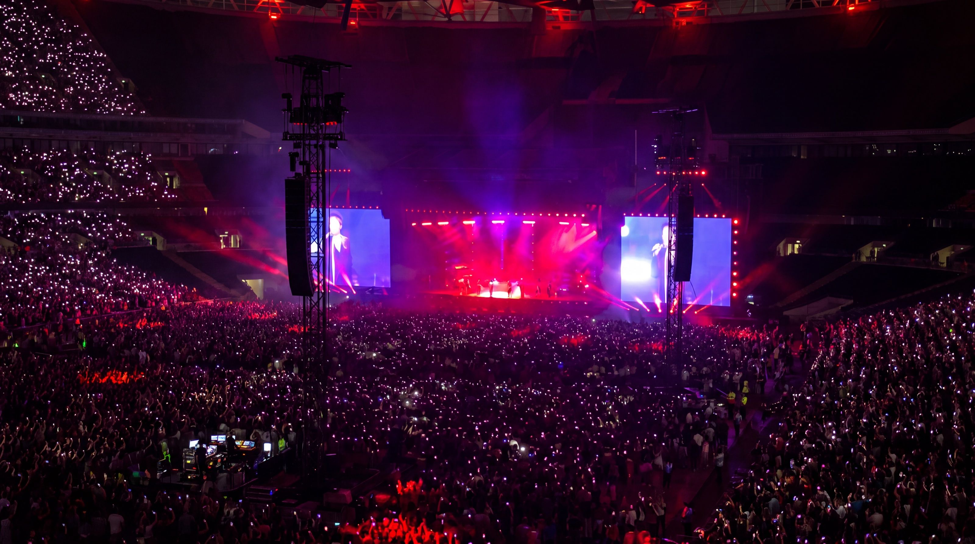 Photo for illustration: a concert at Wembley seen from the seats, with the stage lit in pink and the crowd holding up phone lights