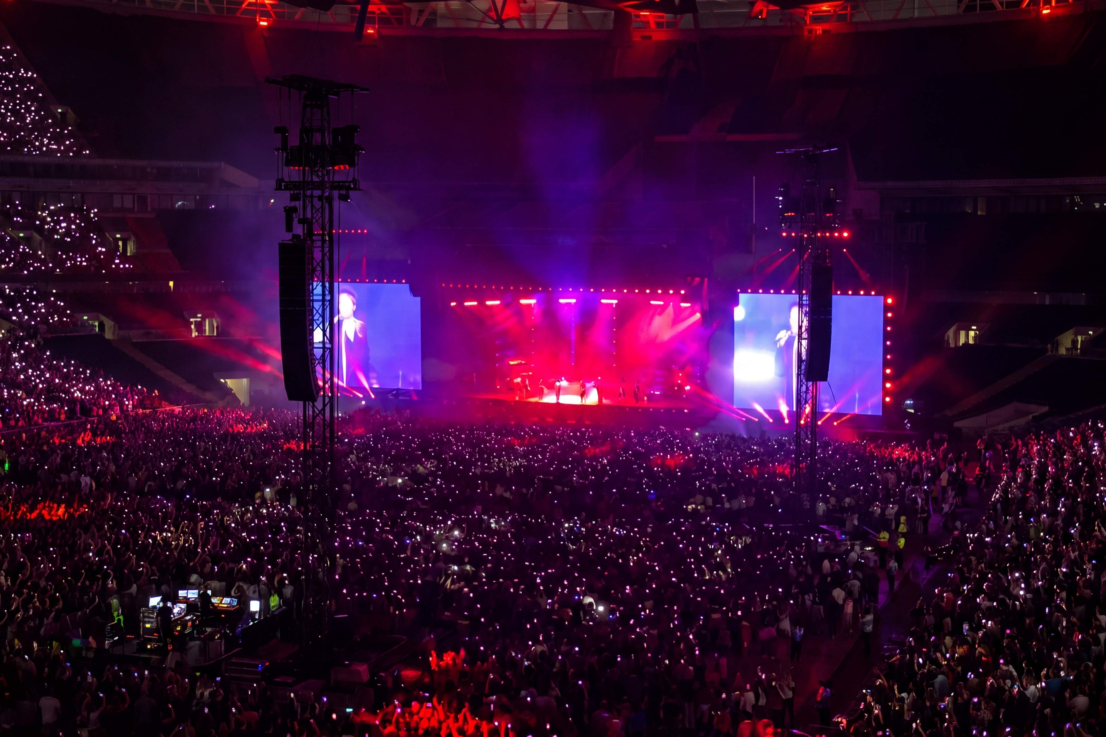 Photo for illustration: a concert at Wembley seen from the seats, with the stage lit in pink and the crowd holding up phone lights