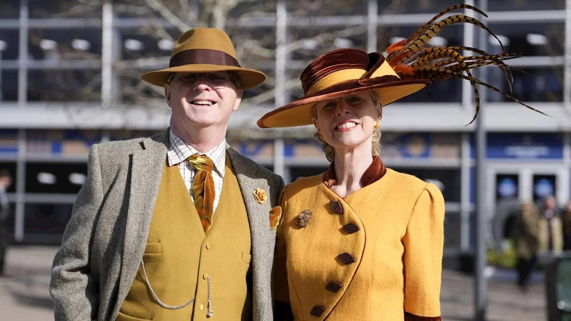 A man and a woman in matching mustard tweed and wide-brimmed hats at Cheltenham Racecourse