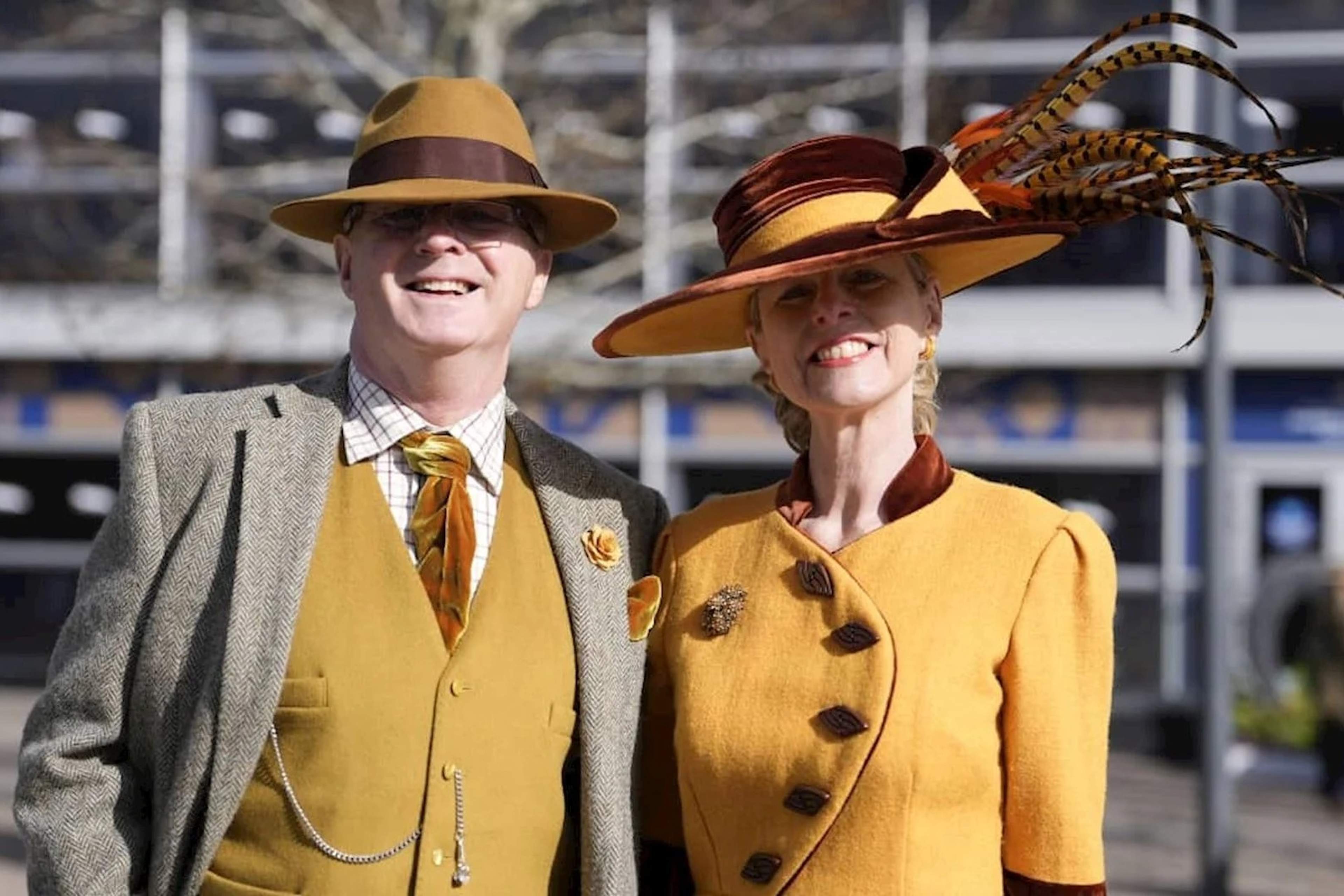 A man and a woman in matching mustard tweed and wide-brimmed hats at Cheltenham Racecourse