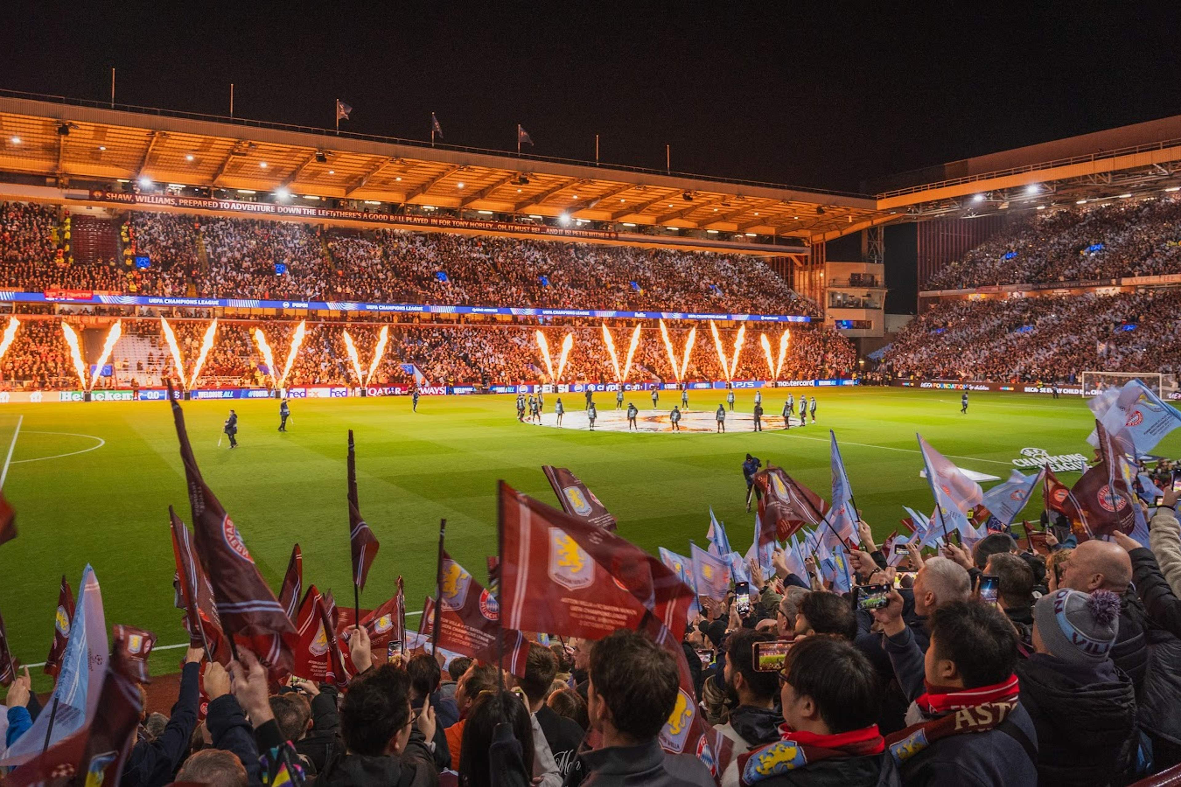 Supporters waving Aston Villa flags beside the pitch during an evening match at Villa Park
