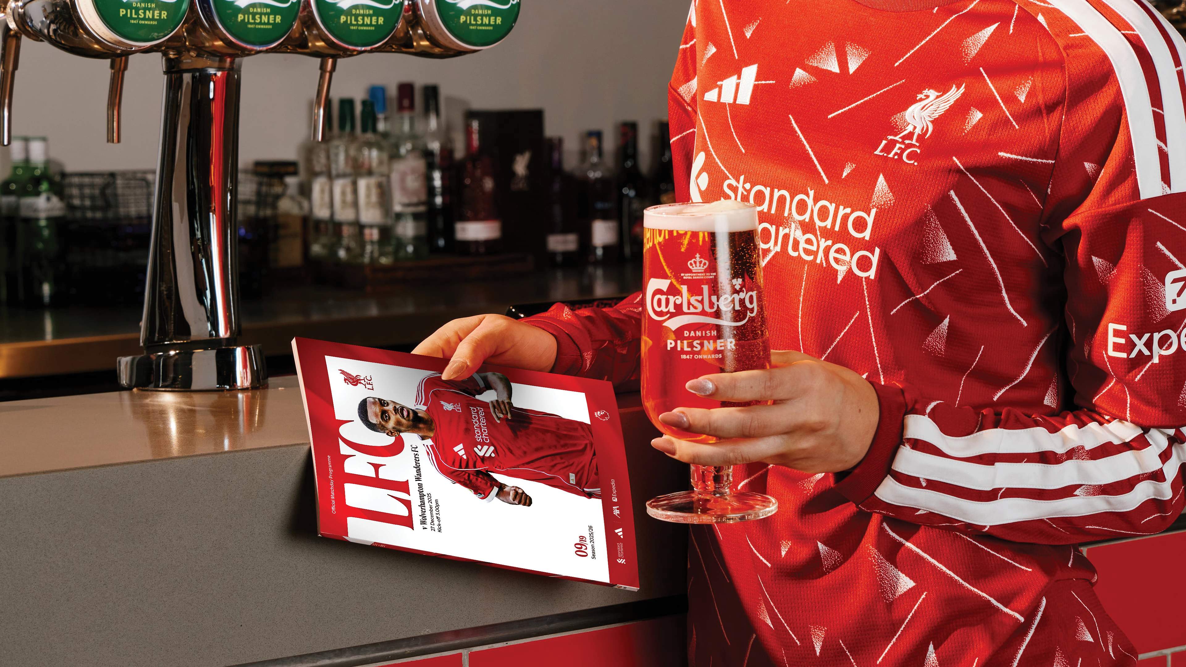 A supporter at the Forever Reds Lounge bar holding a pint and a matchday programme