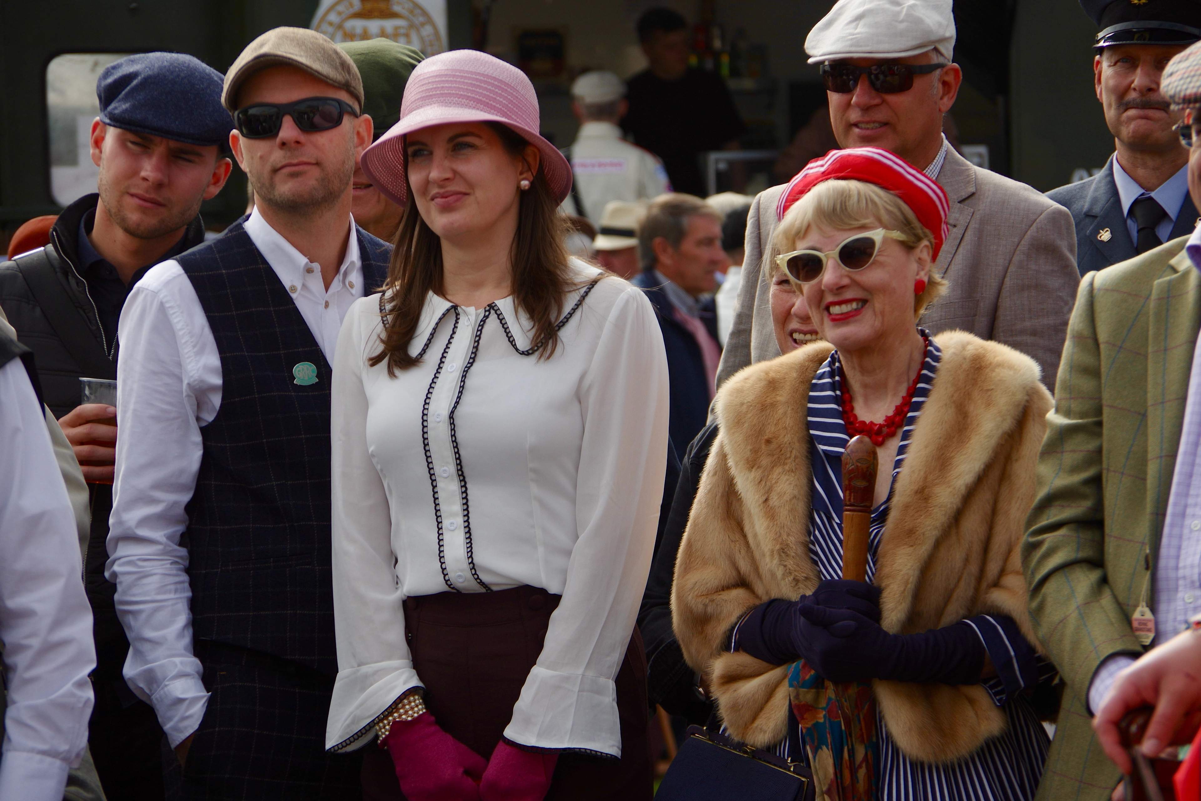 Goodwood Revival spectators in 1940s-60s period dress: flat caps, tweed, cloche hats, fur stoles and cat-eye sunglasses