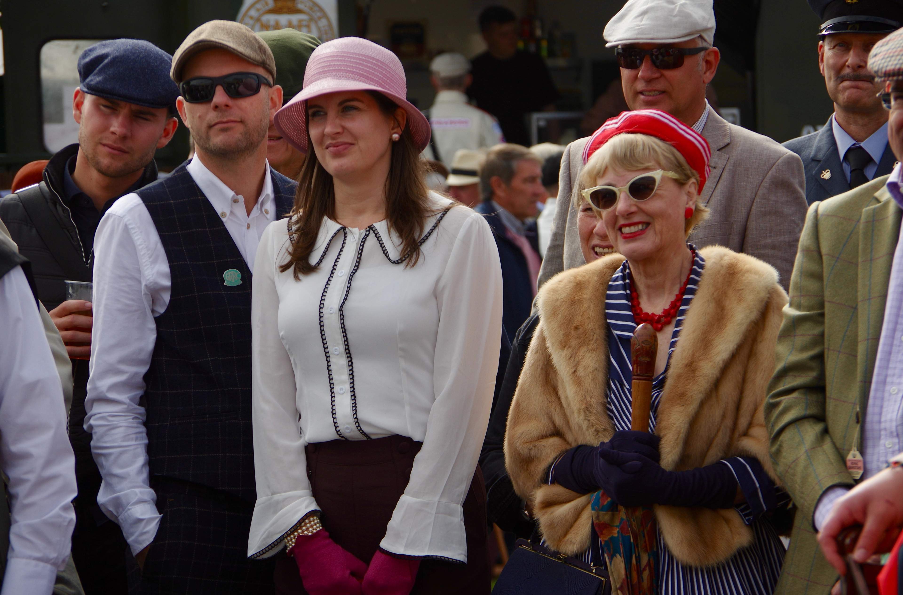Goodwood Revival spectators in 1940s-60s period dress: flat caps, tweed, cloche hats, fur stoles and cat-eye sunglasses