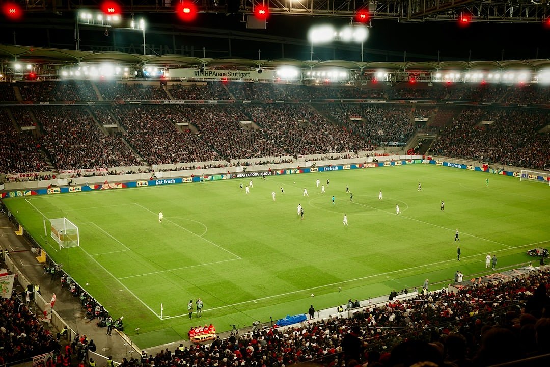 Football match played under floodlights at a packed stadium at night