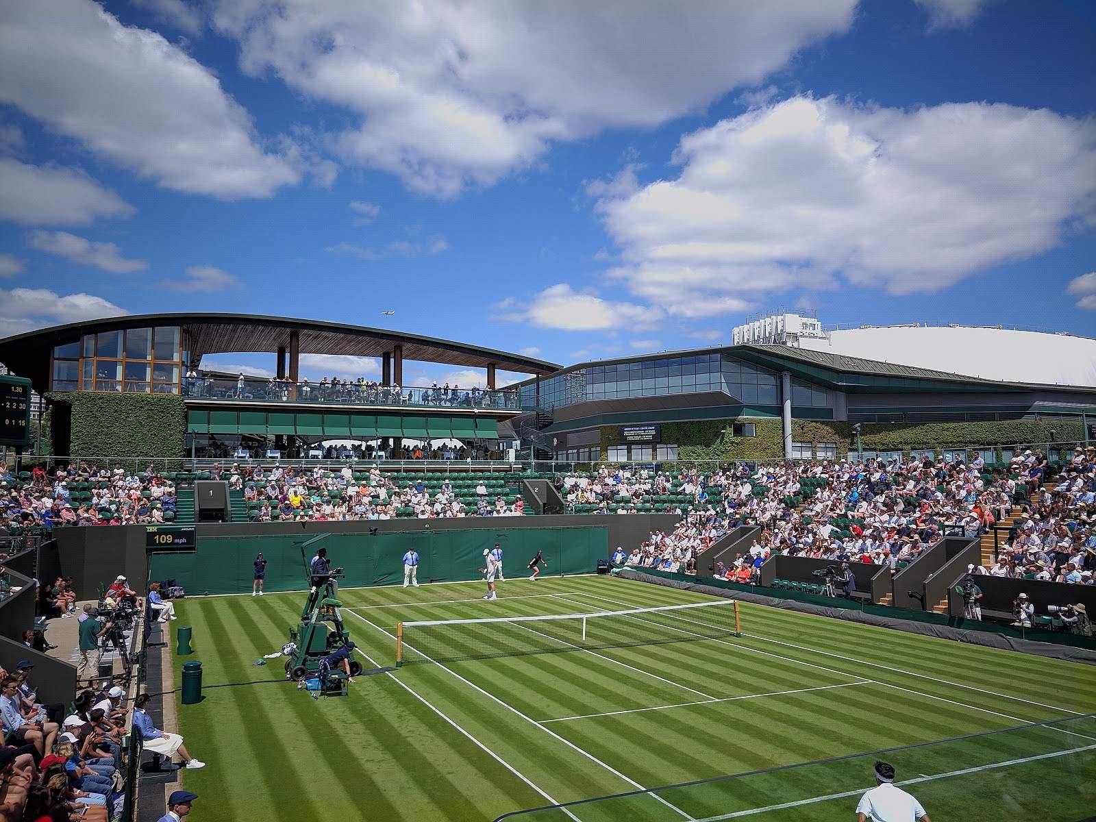 A show court at Wimbledon with striped grass, spectators in the stands and a blue sky