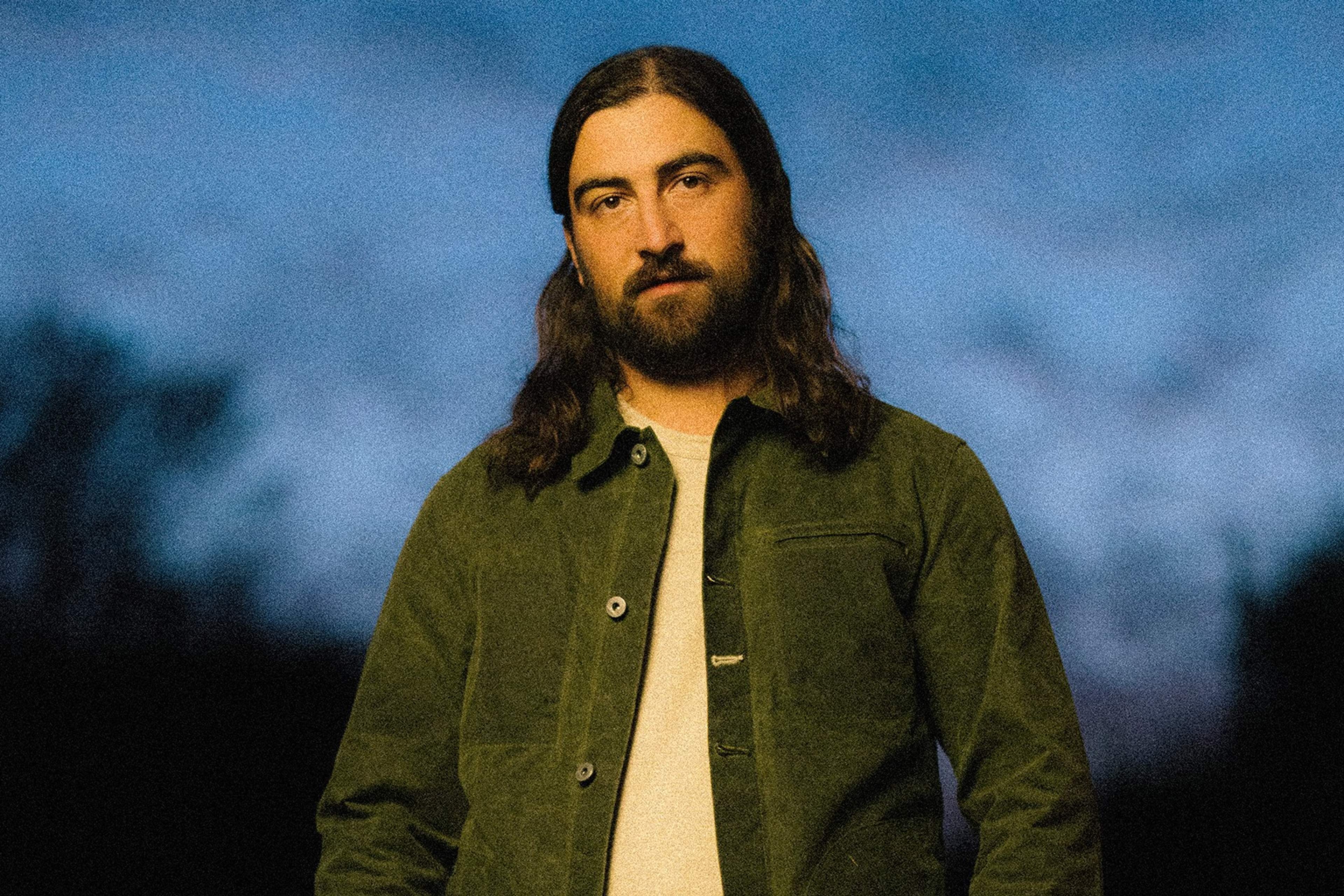 Noah Kahan in a green jacket, photographed outdoors at dusk
