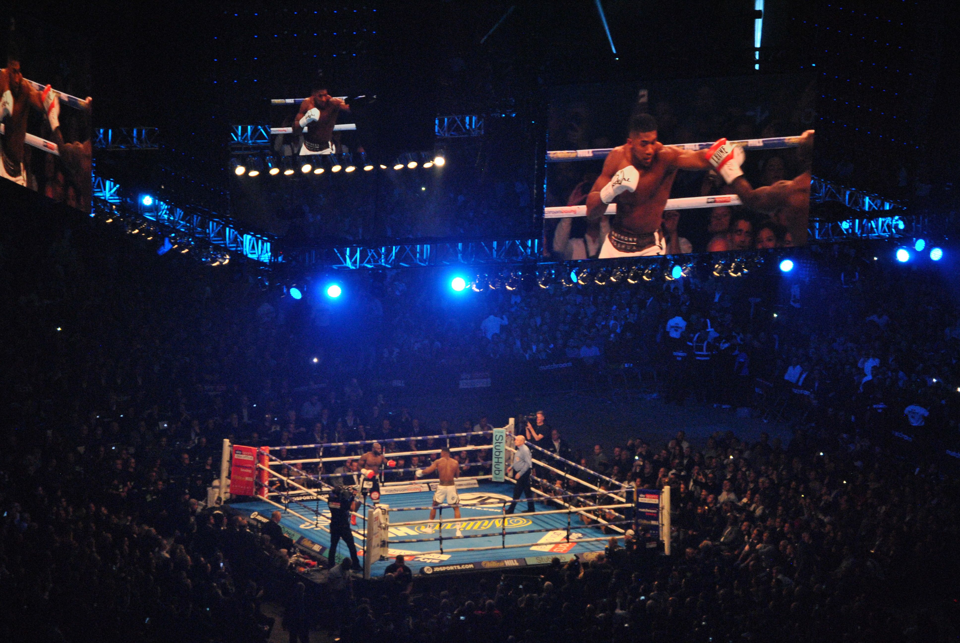 A boxing ring in the middle of a packed Principality Stadium at night, with the fight shown on big screens above it