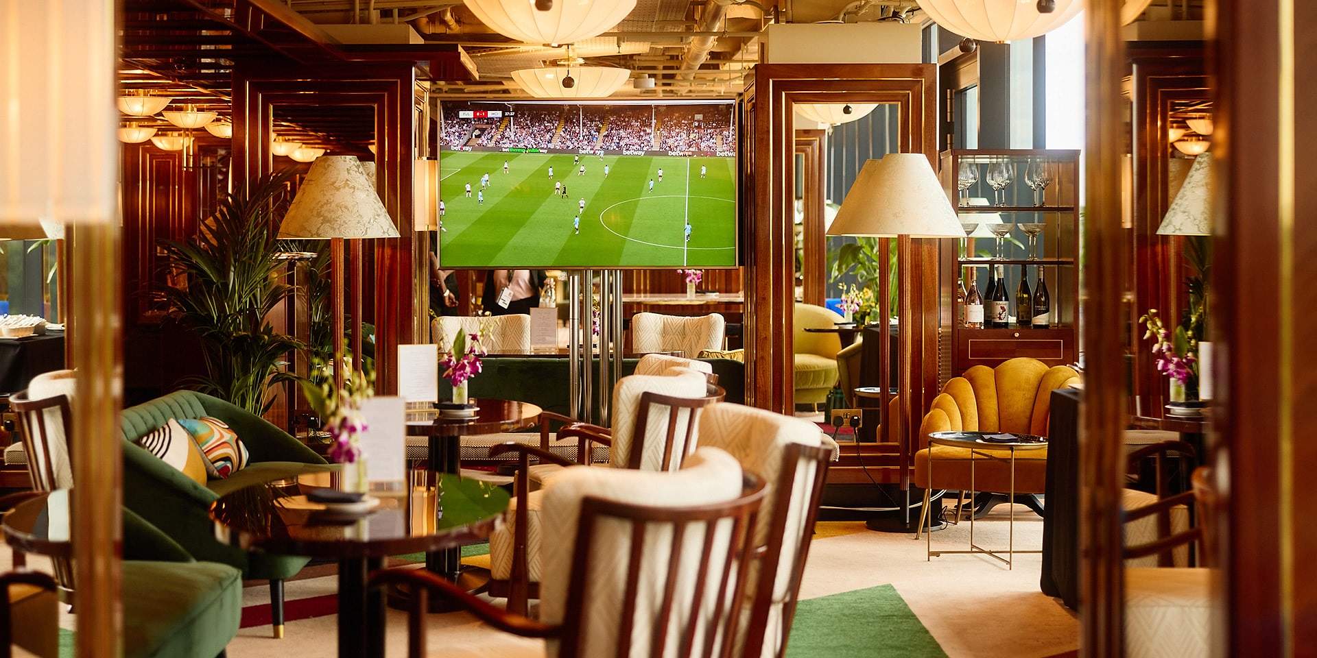 Guests' lounge at The Sky Deck with armchairs and a large screen showing a football match