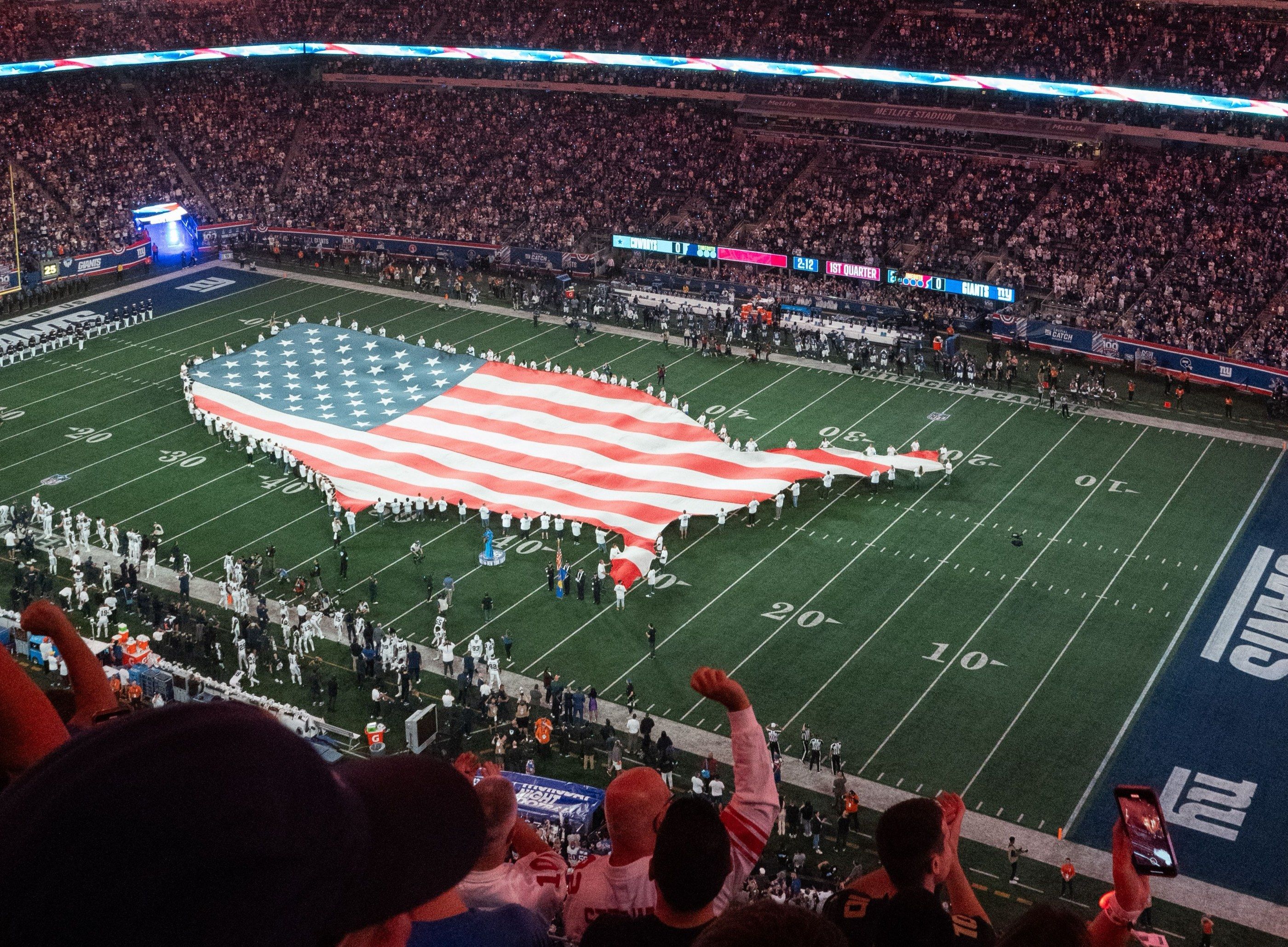 A giant American flag held across an American football field before kick-off