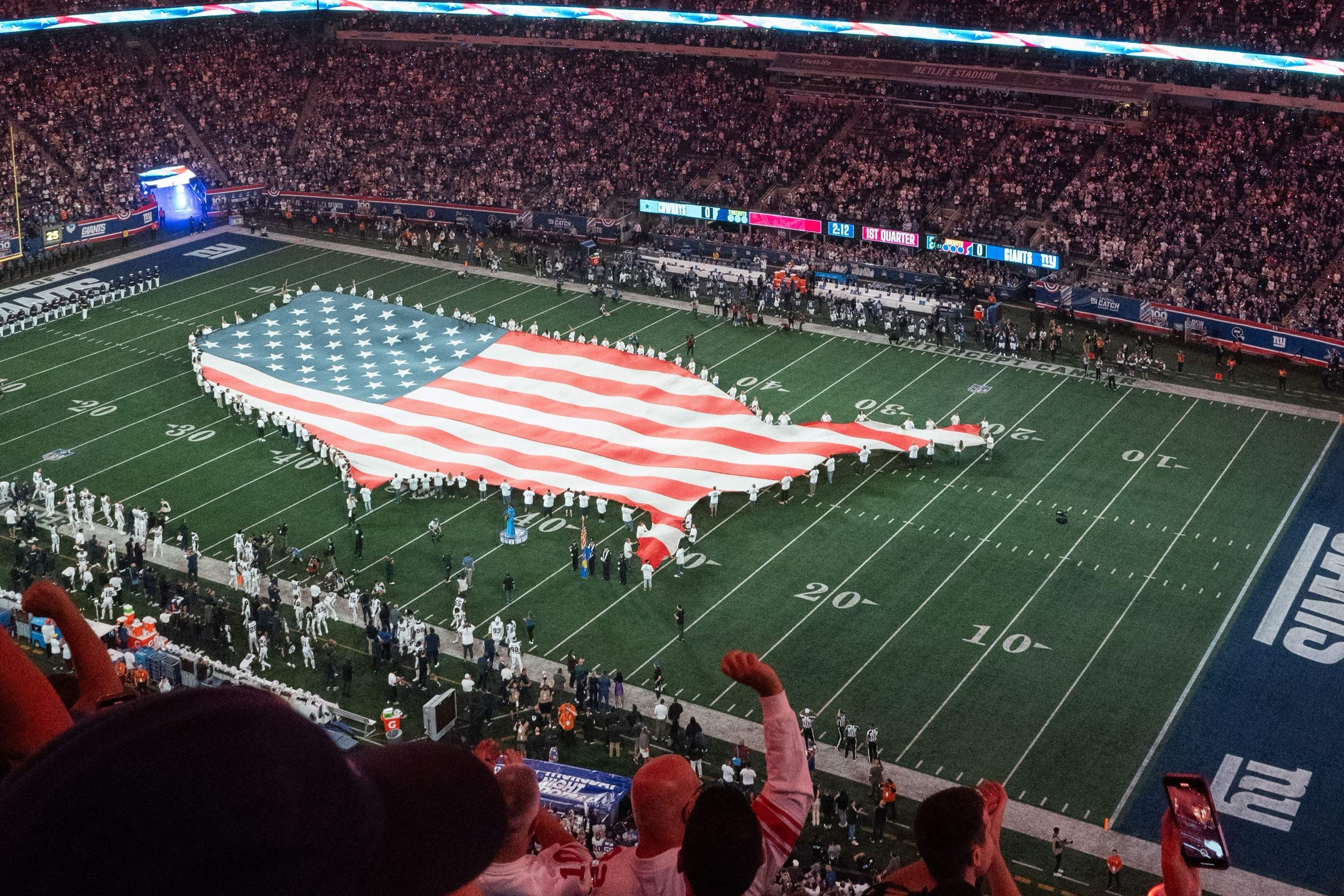 A giant American flag held across an American football field before kick-off