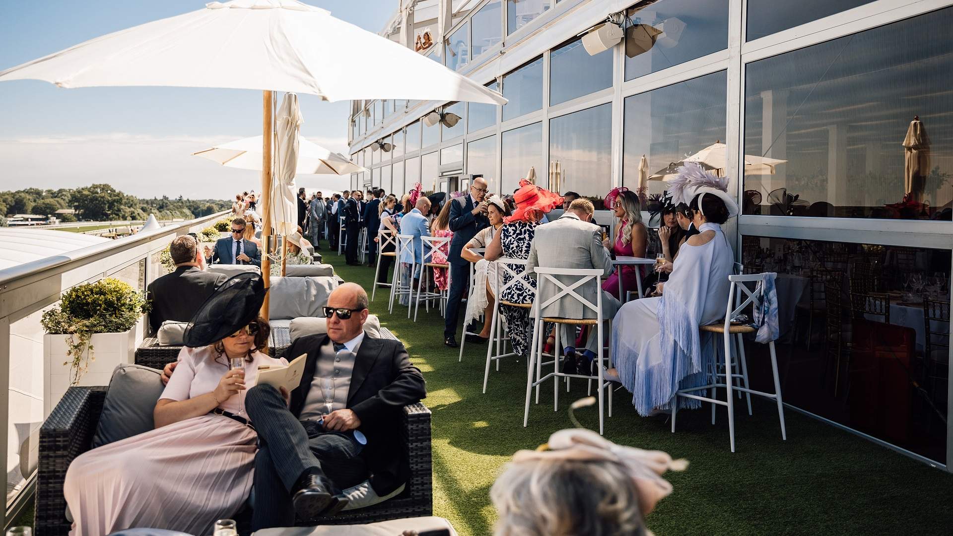 Ladies in colourful headpieces on The Lawn Club hospitality terrace at Royal Ascot