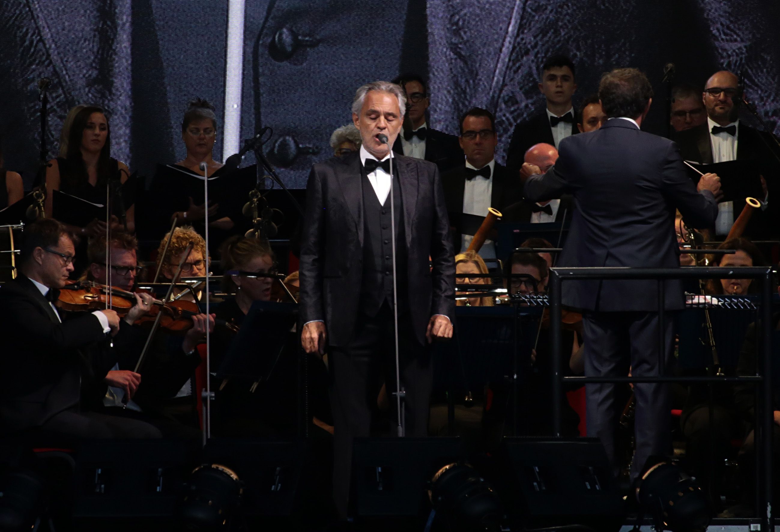 Andrea Bocelli singing with orchestra and choir behind him