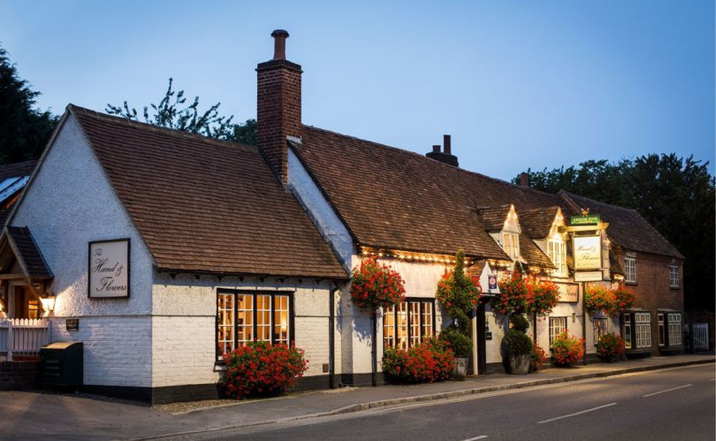 The Hand and Flowers pub in Marlow at dusk, a white-painted building with a tiled roof and hanging baskets