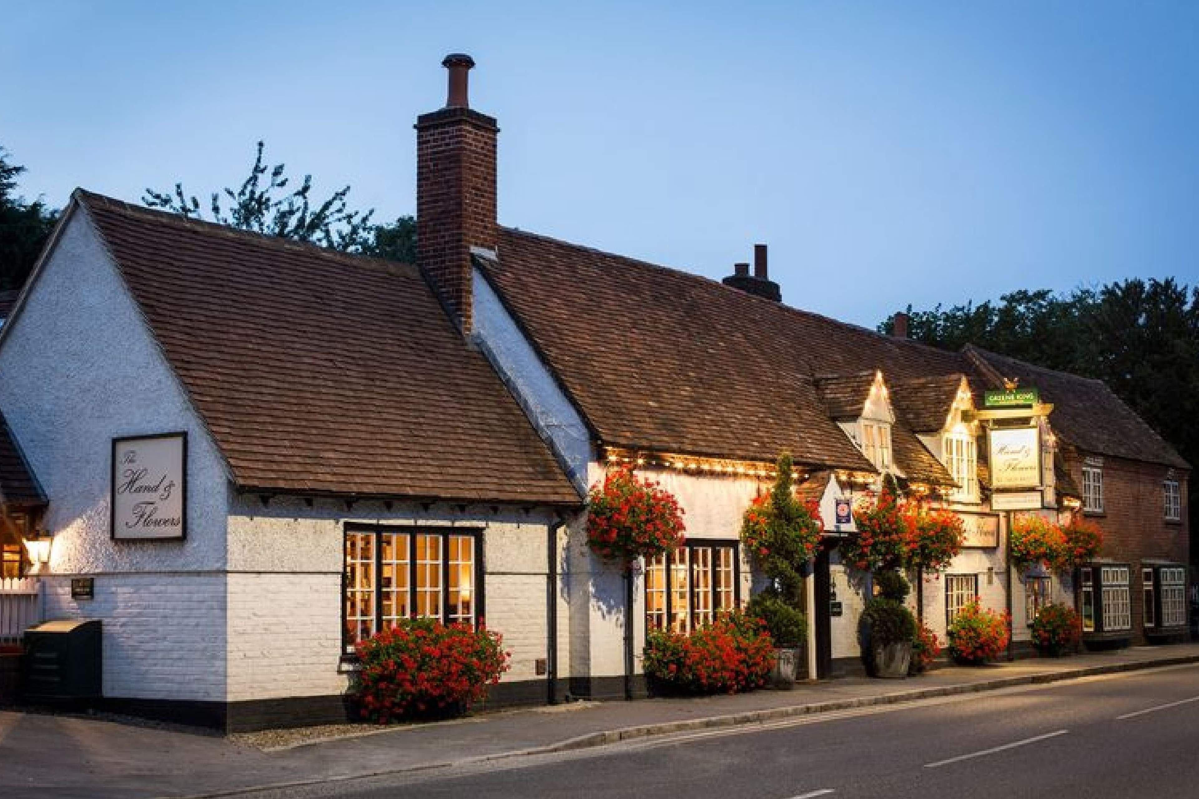 The Hand and Flowers pub in Marlow at dusk, a white-painted building with a tiled roof and hanging baskets
