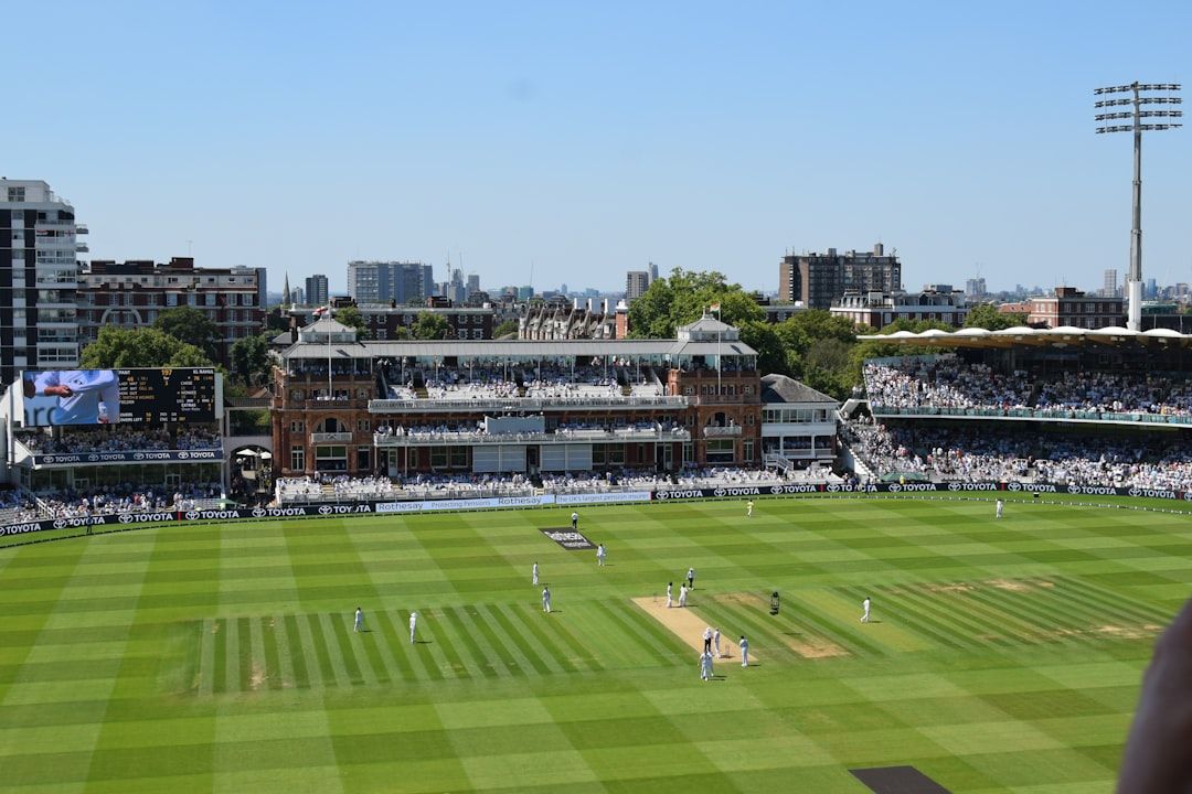 Cricket match underway at a sunny English stadium