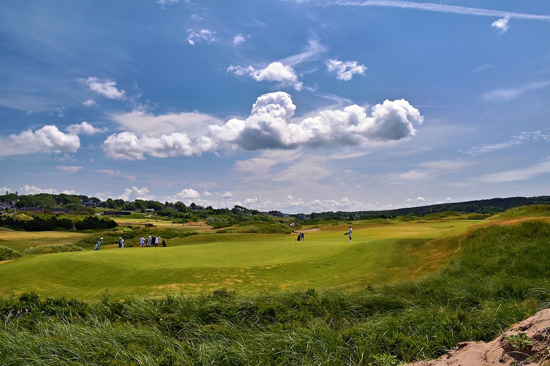 Golfers on a green links course under a cloudy sky