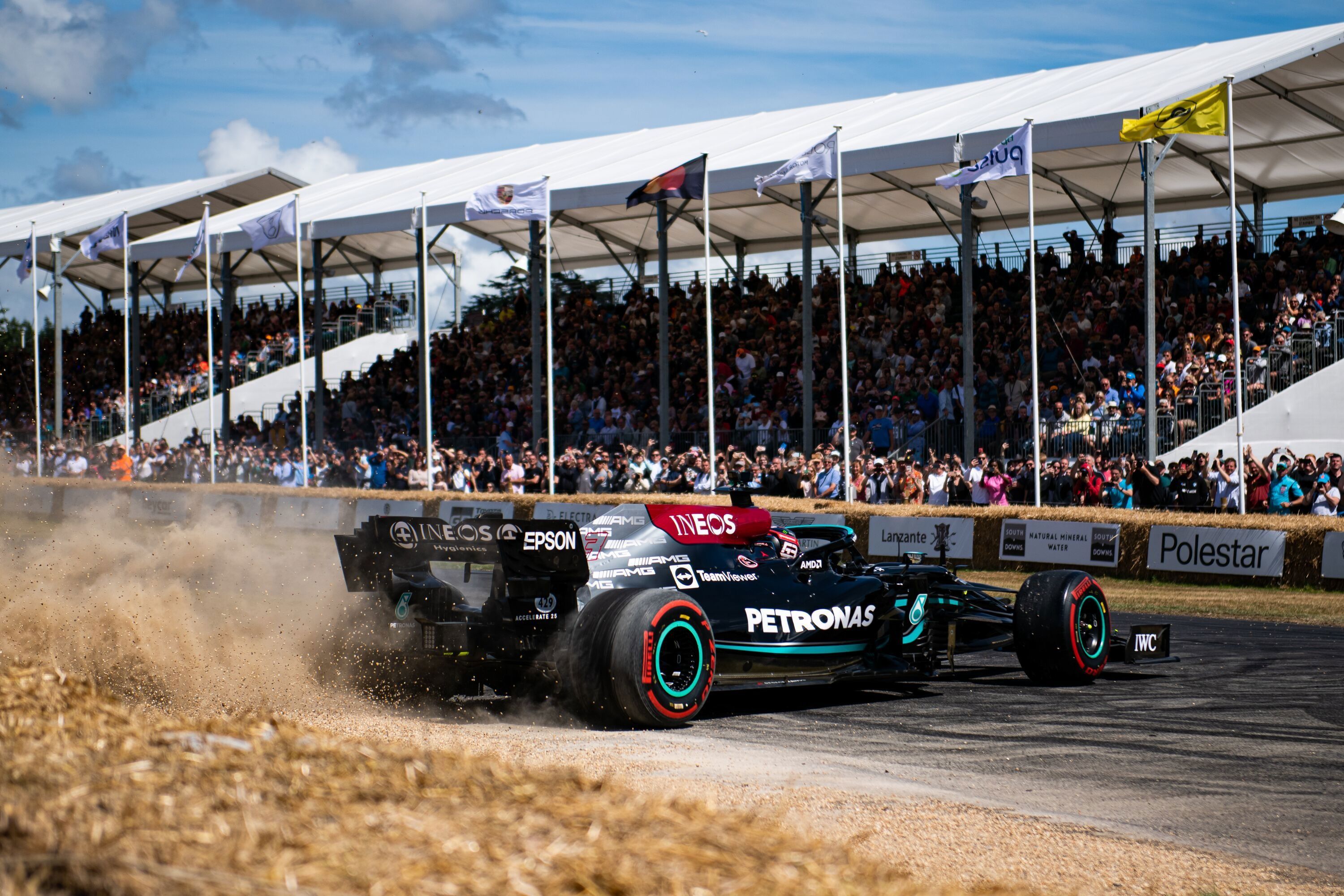 A Mercedes Formula 1 car kicks up straw in front of packed covered grandstands at the Goodwood Festival of Speed