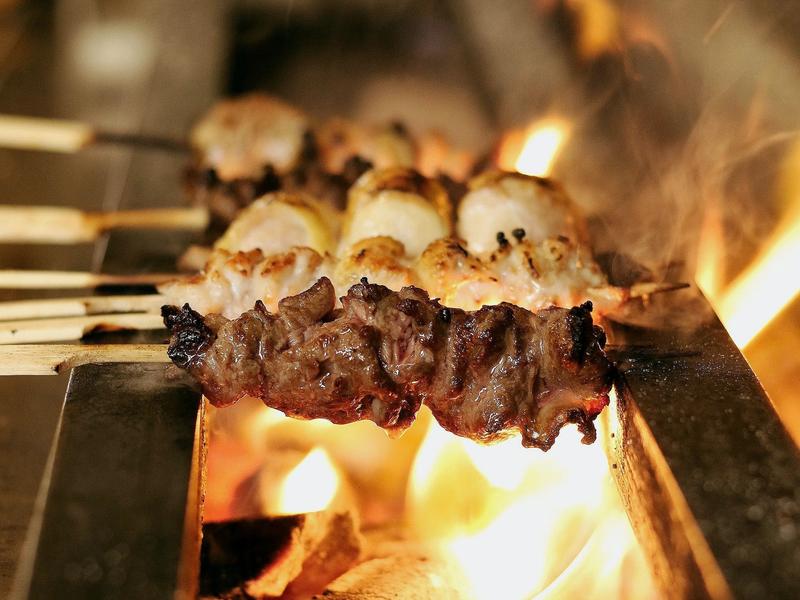 Chicken skewers sizzling over an open charcoal grill at Birdman yakitori bar in Athens — the intimate counter dining experience near Syntagma