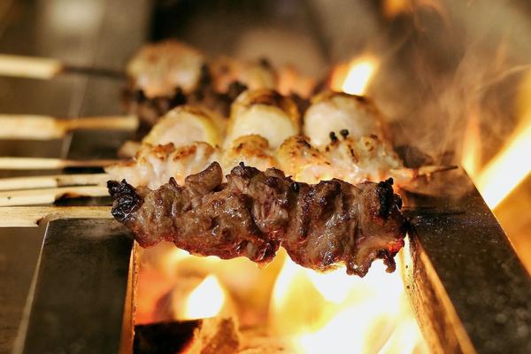 Chicken skewers sizzling over an open charcoal grill at Birdman yakitori bar in Athens — the intimate counter dining experience near Syntagma