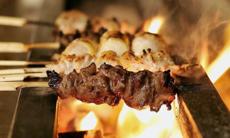 Chicken skewers sizzling over an open charcoal grill at Birdman yakitori bar in Athens — the intimate counter dining experience near Syntagma