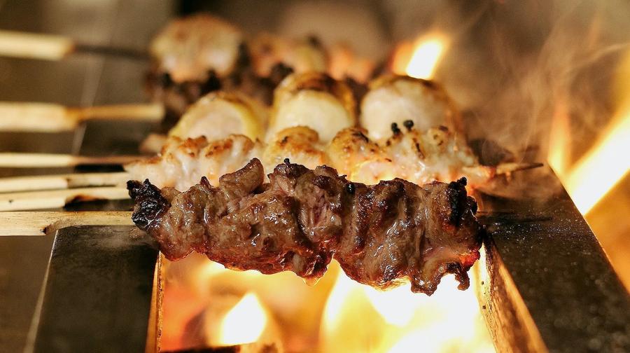 Chicken skewers sizzling over an open charcoal grill at Birdman yakitori bar in Athens — the intimate counter dining experience near Syntagma