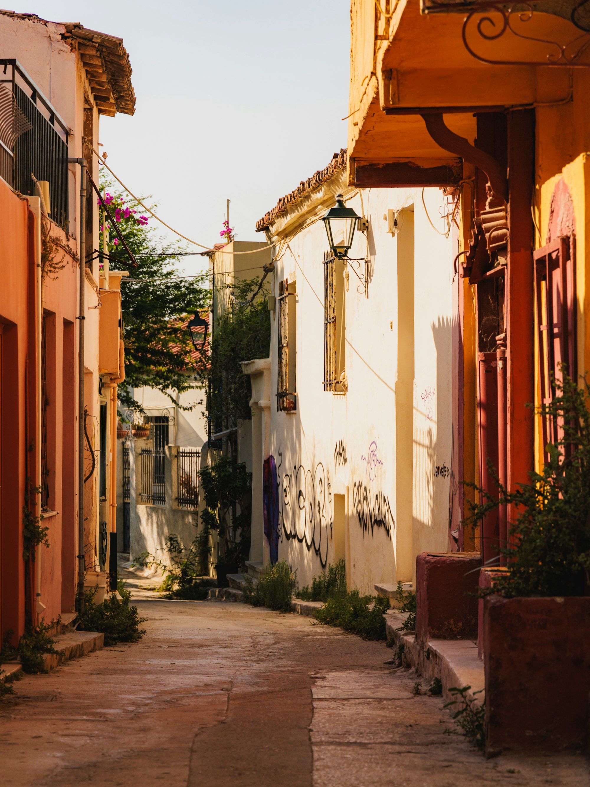 A hidden alley in the Plaka district of Athens, a lamp post at its centre, terracotta pots lining the walls