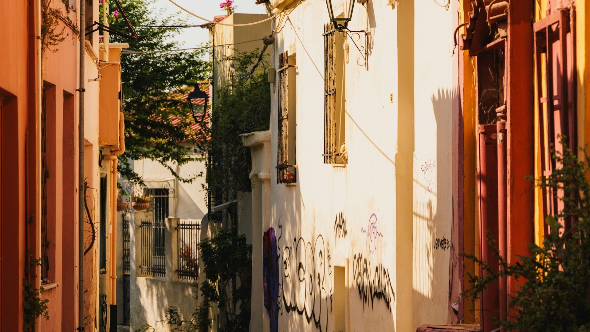 A hidden alley in the Plaka district of Athens, a lamp post at its centre, terracotta pots lining the walls