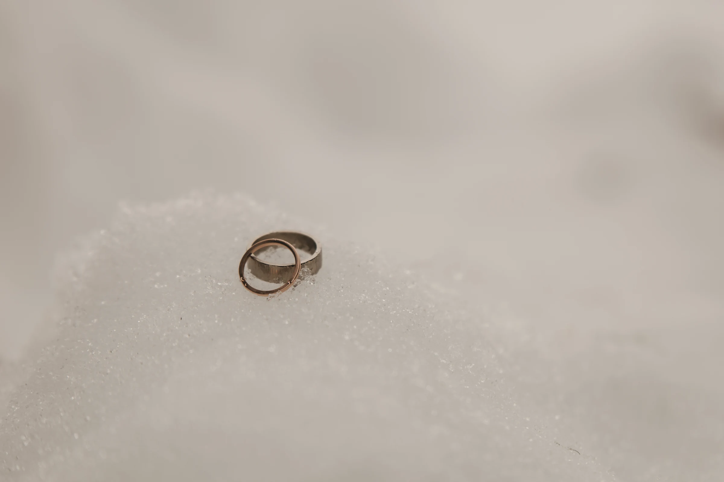 Two intertwined silver rings rest gently on a soft mound of snow, symbolizing love and unity amidst a serene, wintry landscape.