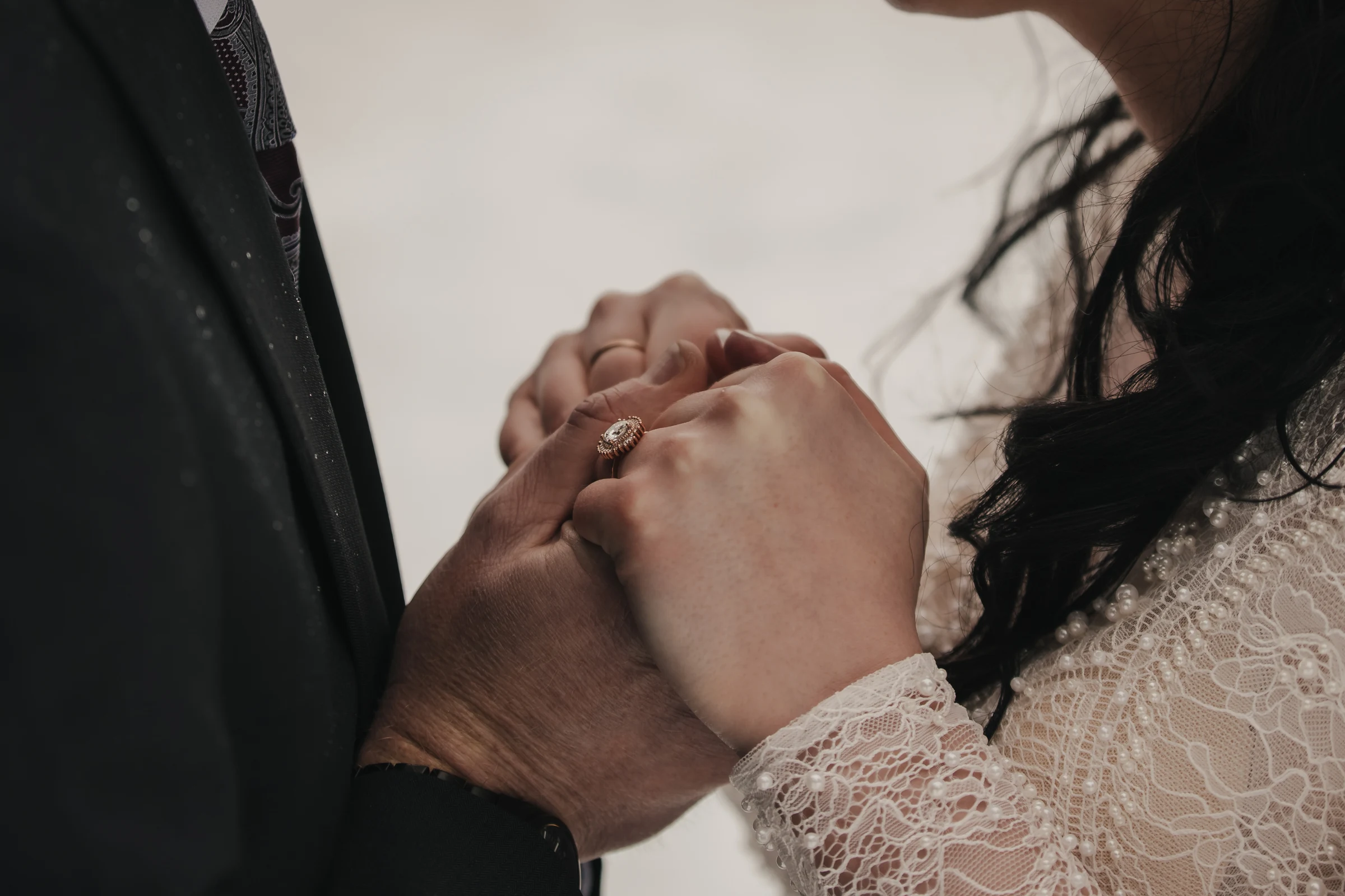 Close-up of a couple holding hands, highlighting a lace wedding dress and a ring. The tone conveys intimacy and love, symbolizing unity.