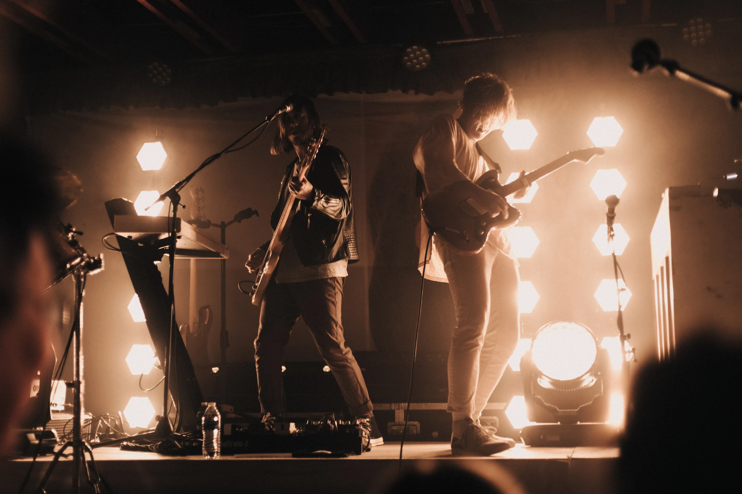 A dynamic live band performance with guitarists under warm, glowing lights, creating a vibrant, energetic atmosphere with a modern rock vibe.