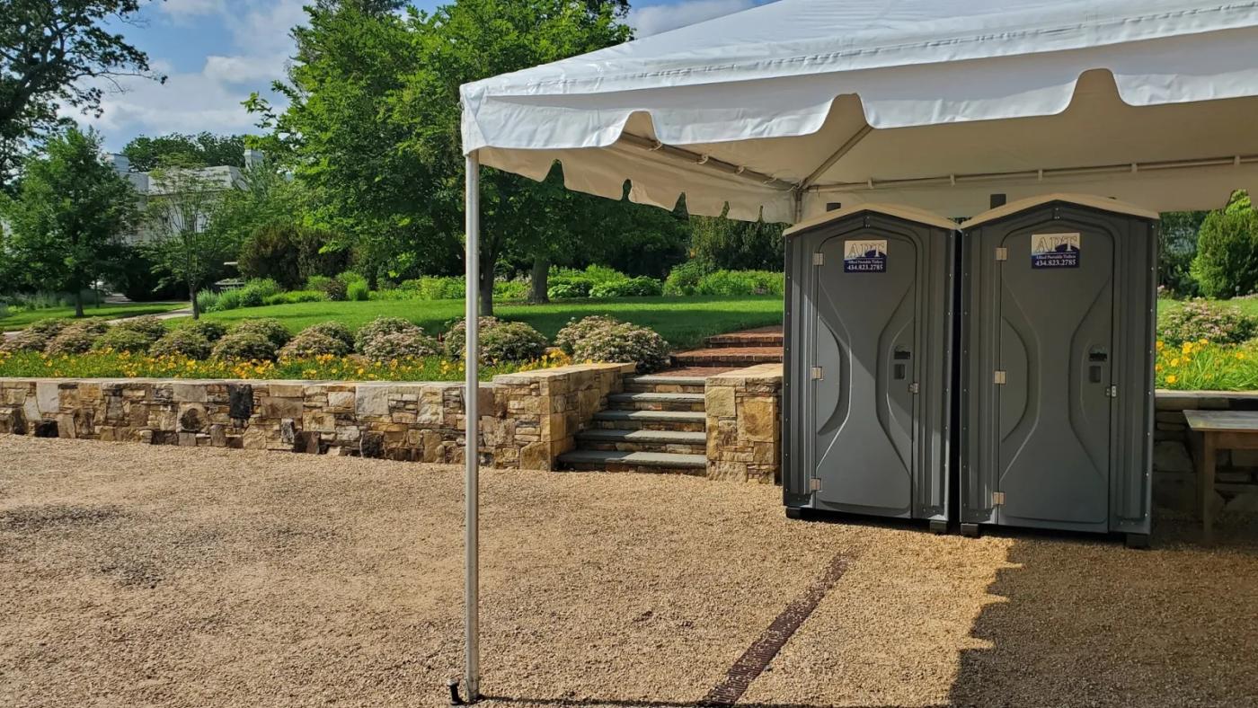 Two APT portable toilets positioned under a white event tent at a garden venue