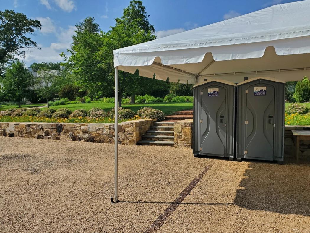 Two APT portable toilets positioned under a white event tent at a garden venue