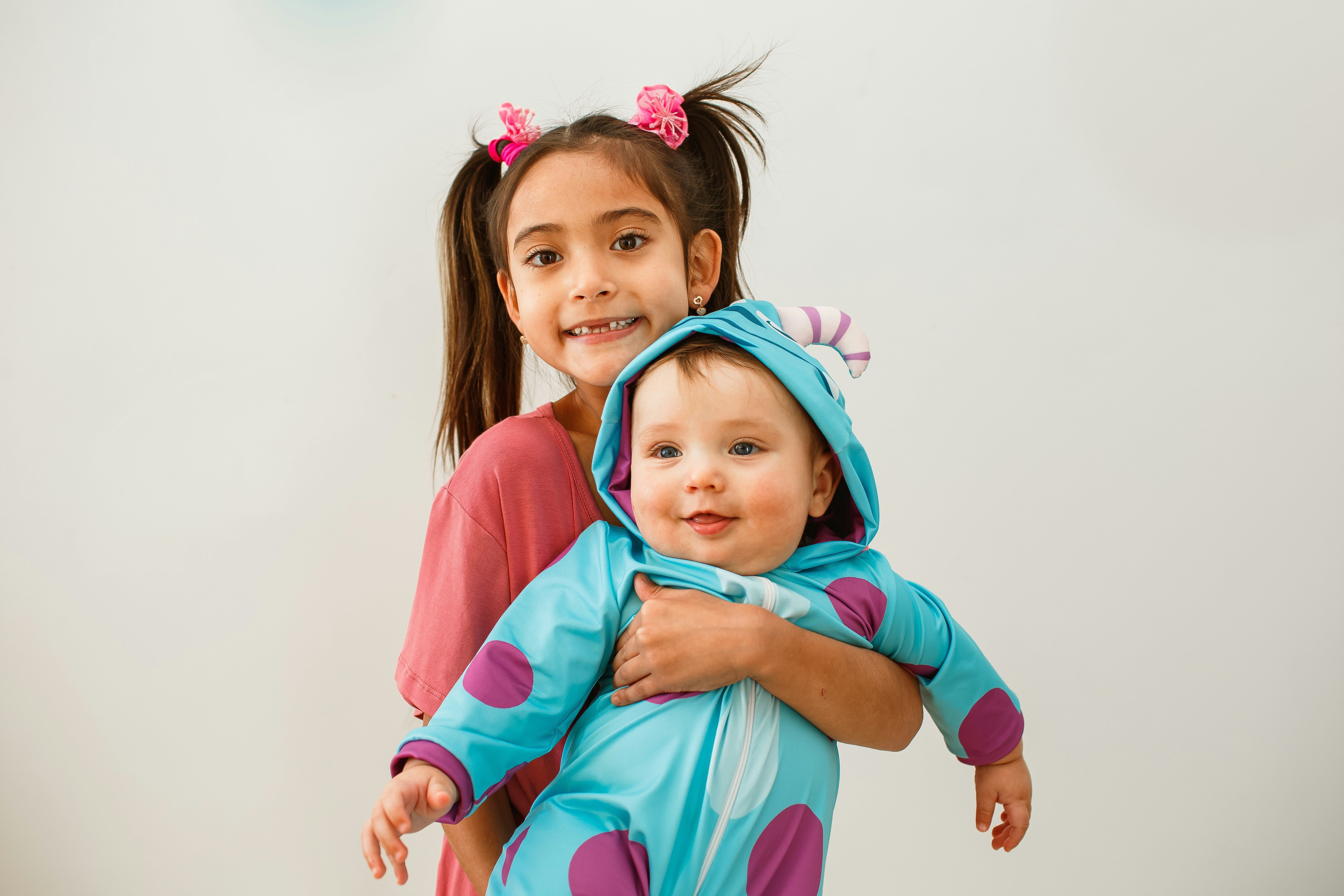 Smiling girl in pigtails holding a baby in a blue and purple spotted monster costume during Halloween parenting time.