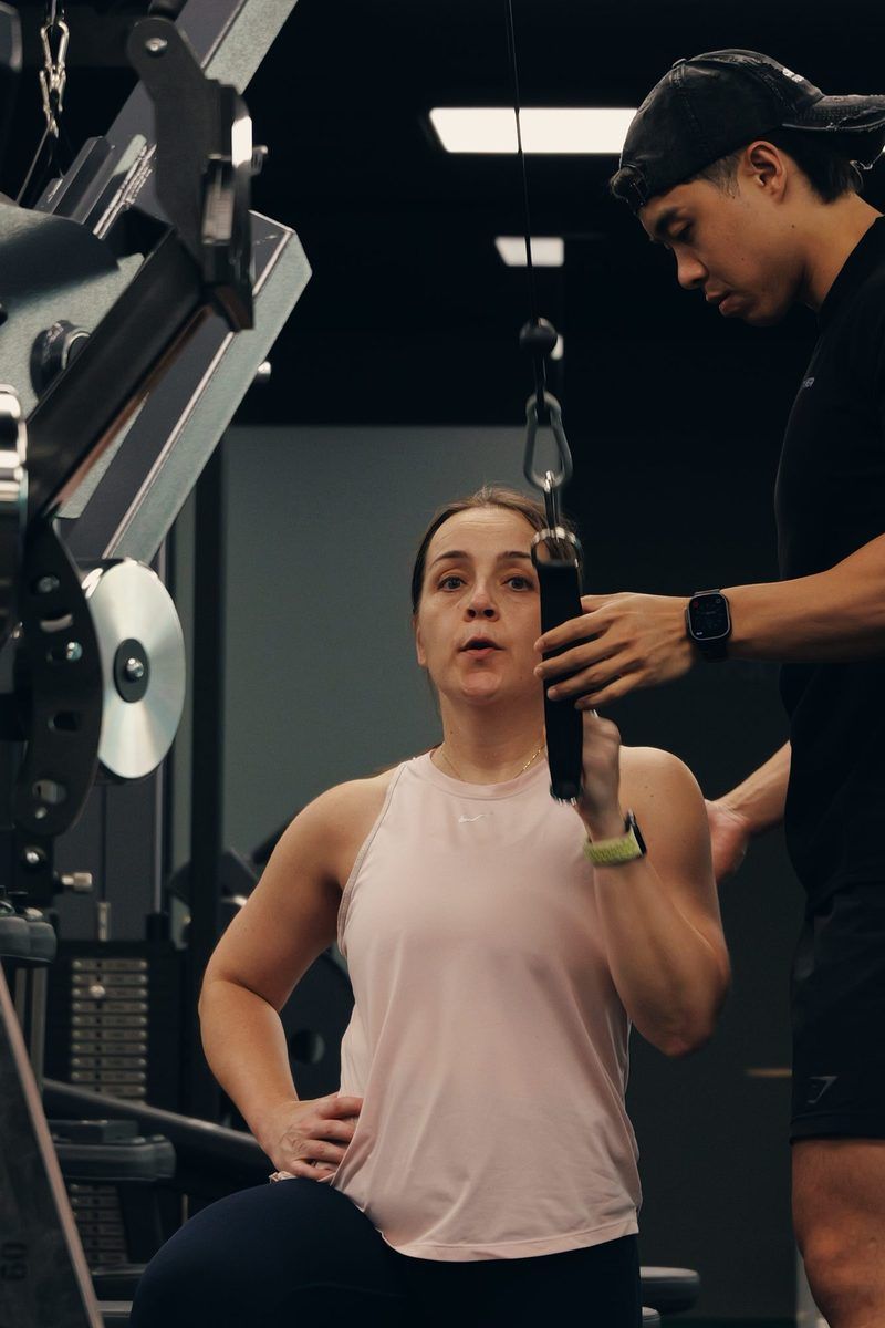 A woman in her 40s performs a coached cable exercise with a Catalyst trainer in Singapore