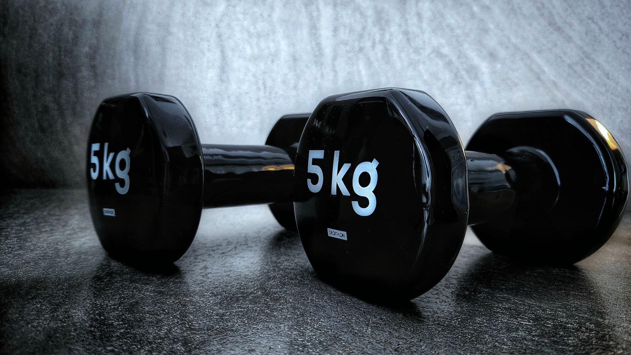 Two five-kilogram dumbbells resting on a dark studio floor