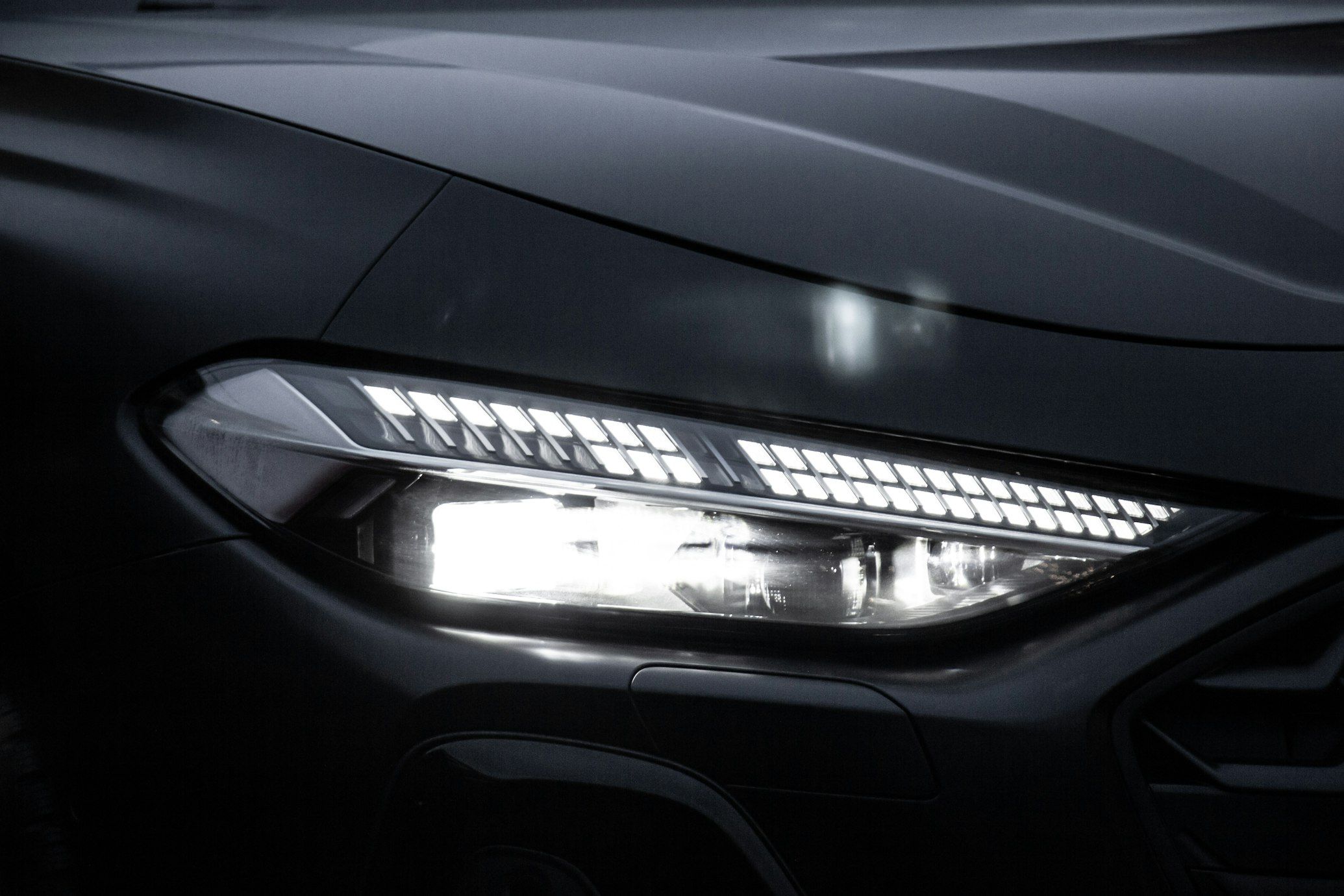 Close-up of an illuminated Audi headlight with a segmented daytime running-light pattern.