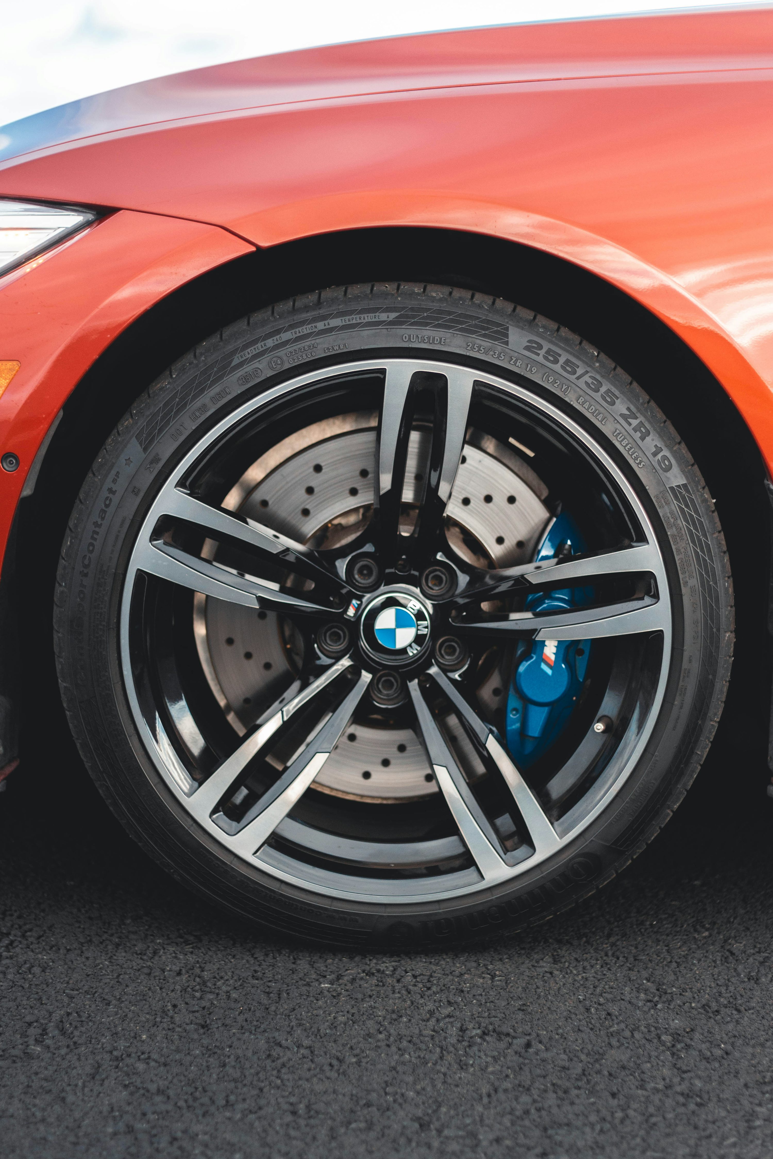 Close-up of a BMW alloy wheel, tyre and blue M brake caliper beneath an orange front wing.