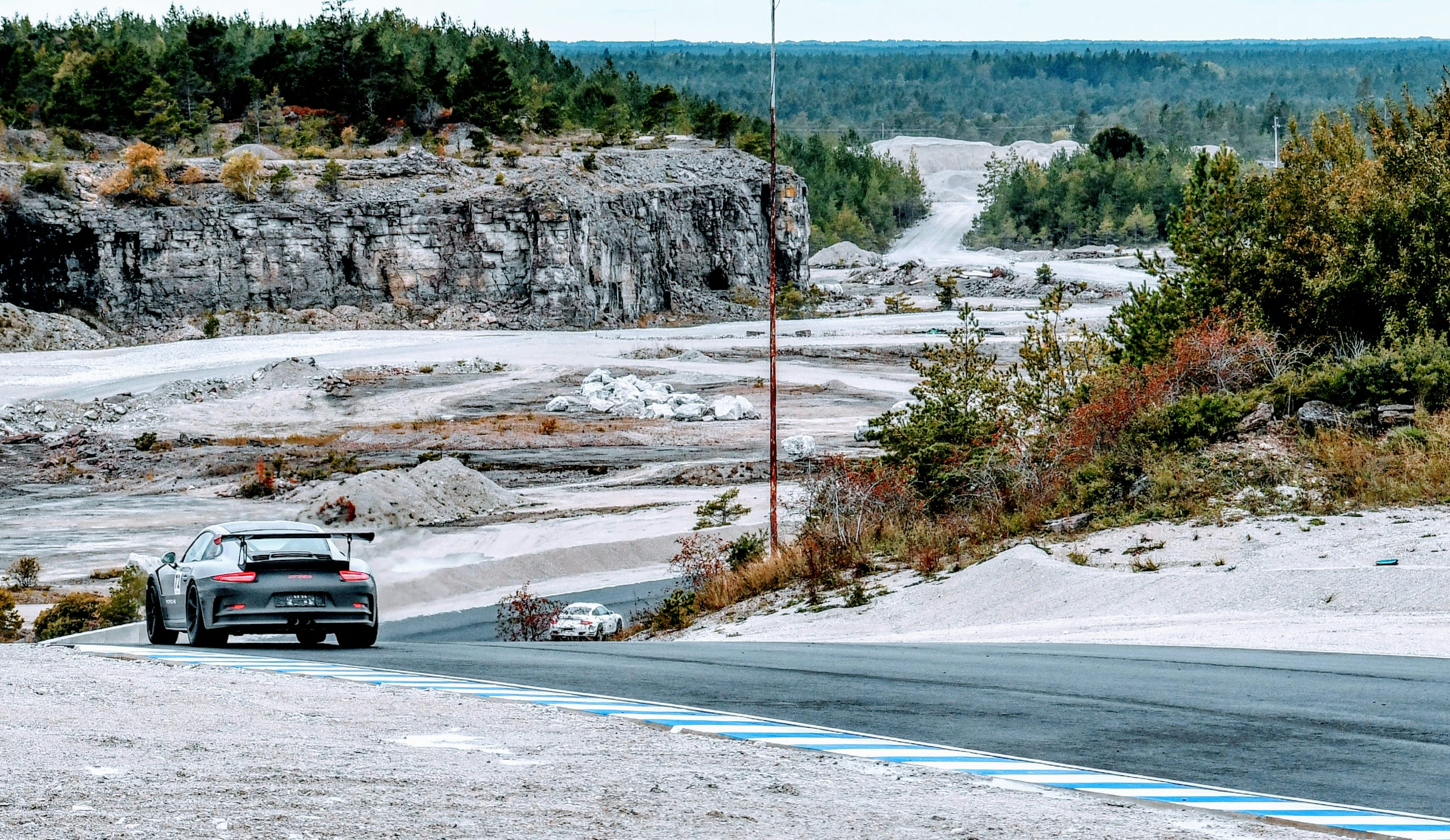 Porsche 911 GT3 RS rounding a bend on a circuit surrounded by pale rock and forest.