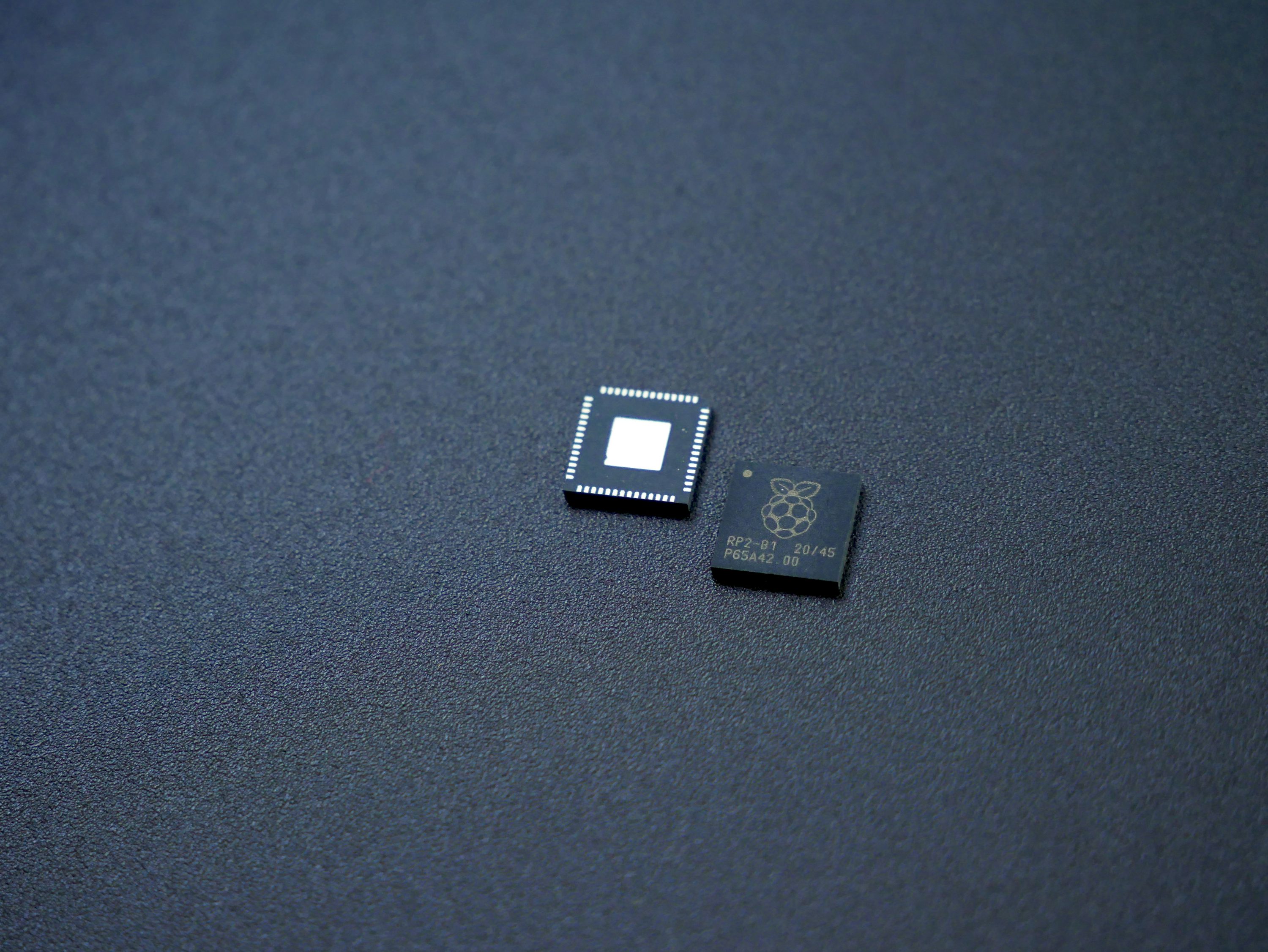 Two semiconductor microcontroller chips on a dark surface, showing the marked upper face and underside contacts.