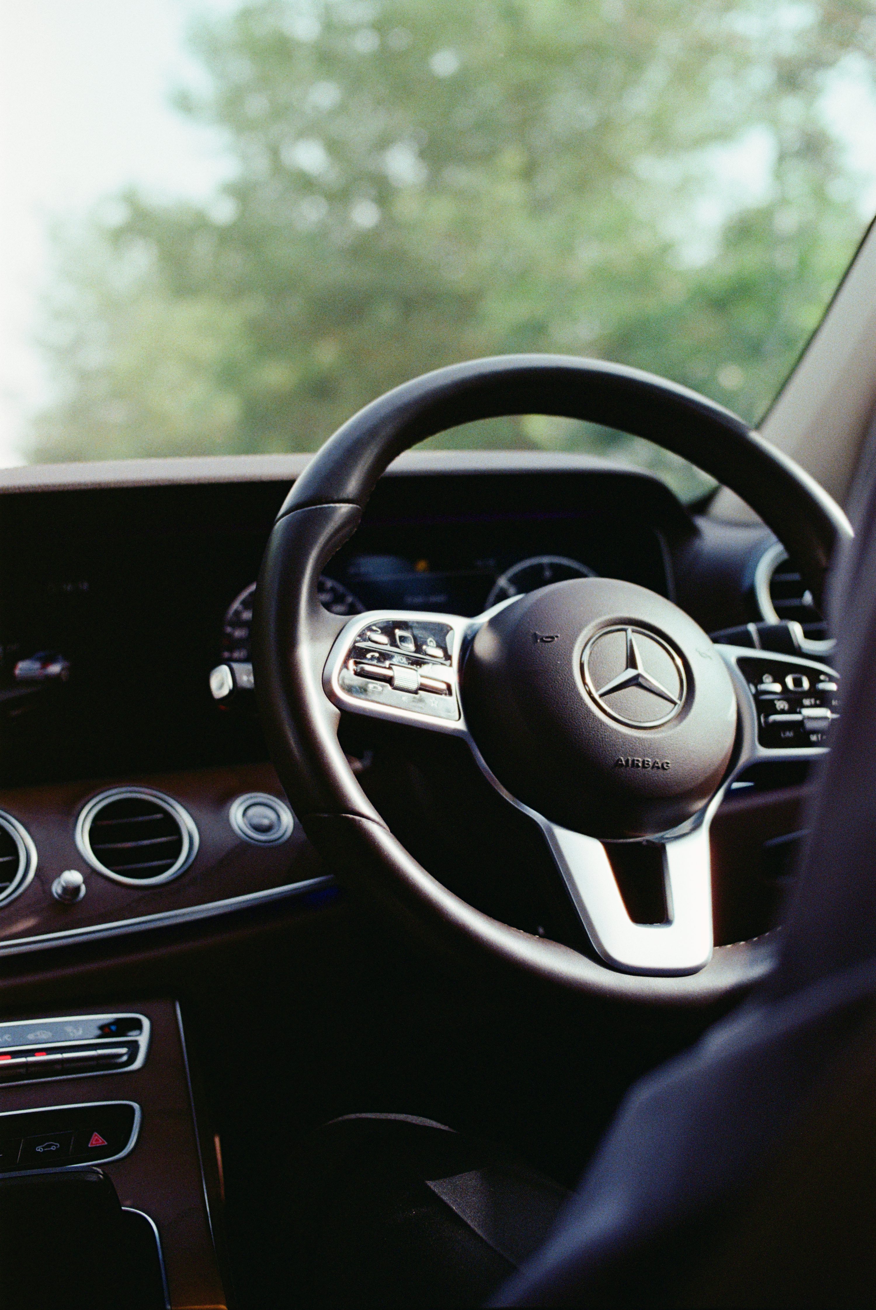 Mercedes-Benz steering wheel with multifunction controls in front of a wide dashboard display.
