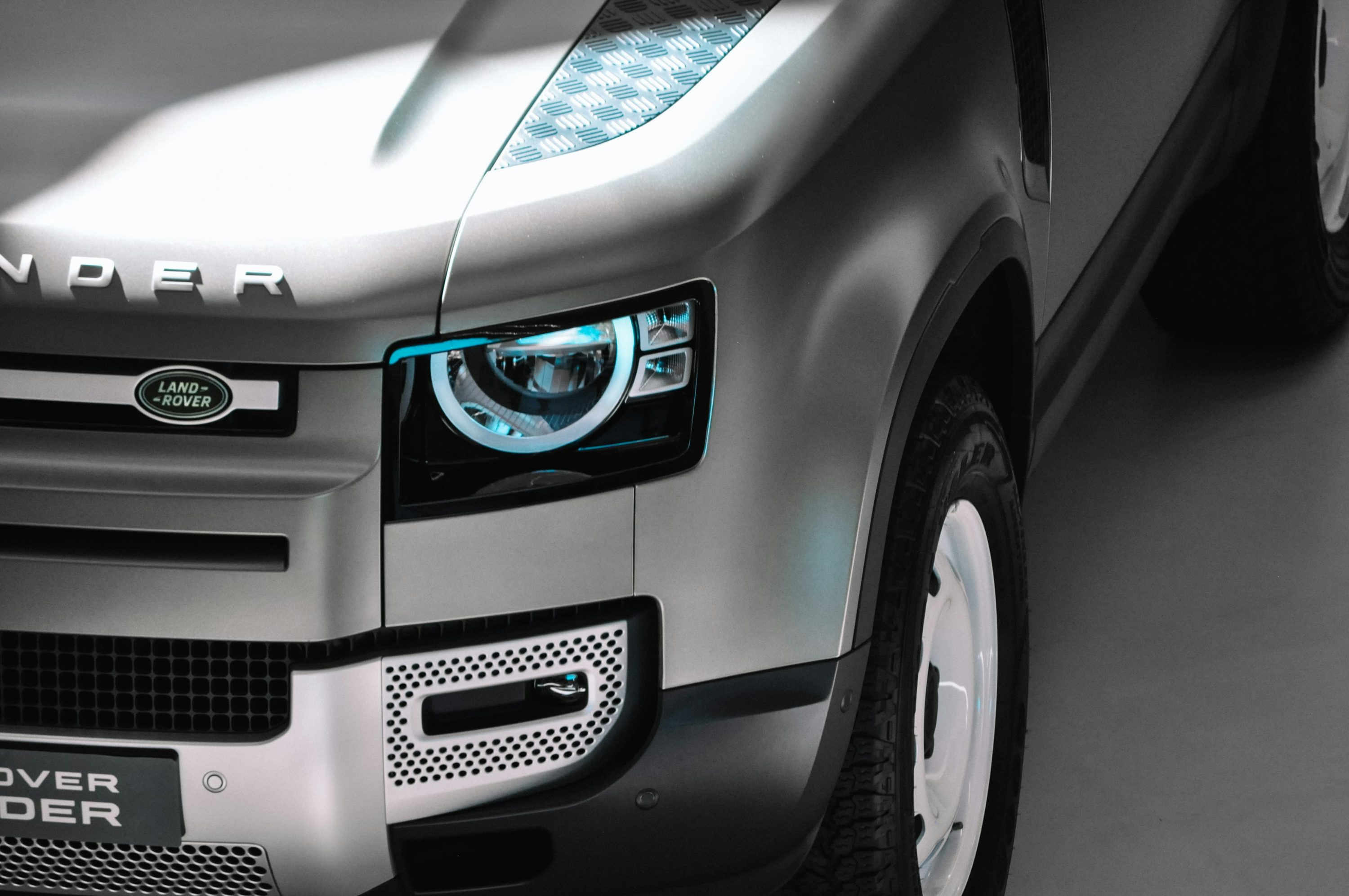 Close-up of a silver Land Rover Defender showing its headlight, front wing and white steel wheel.