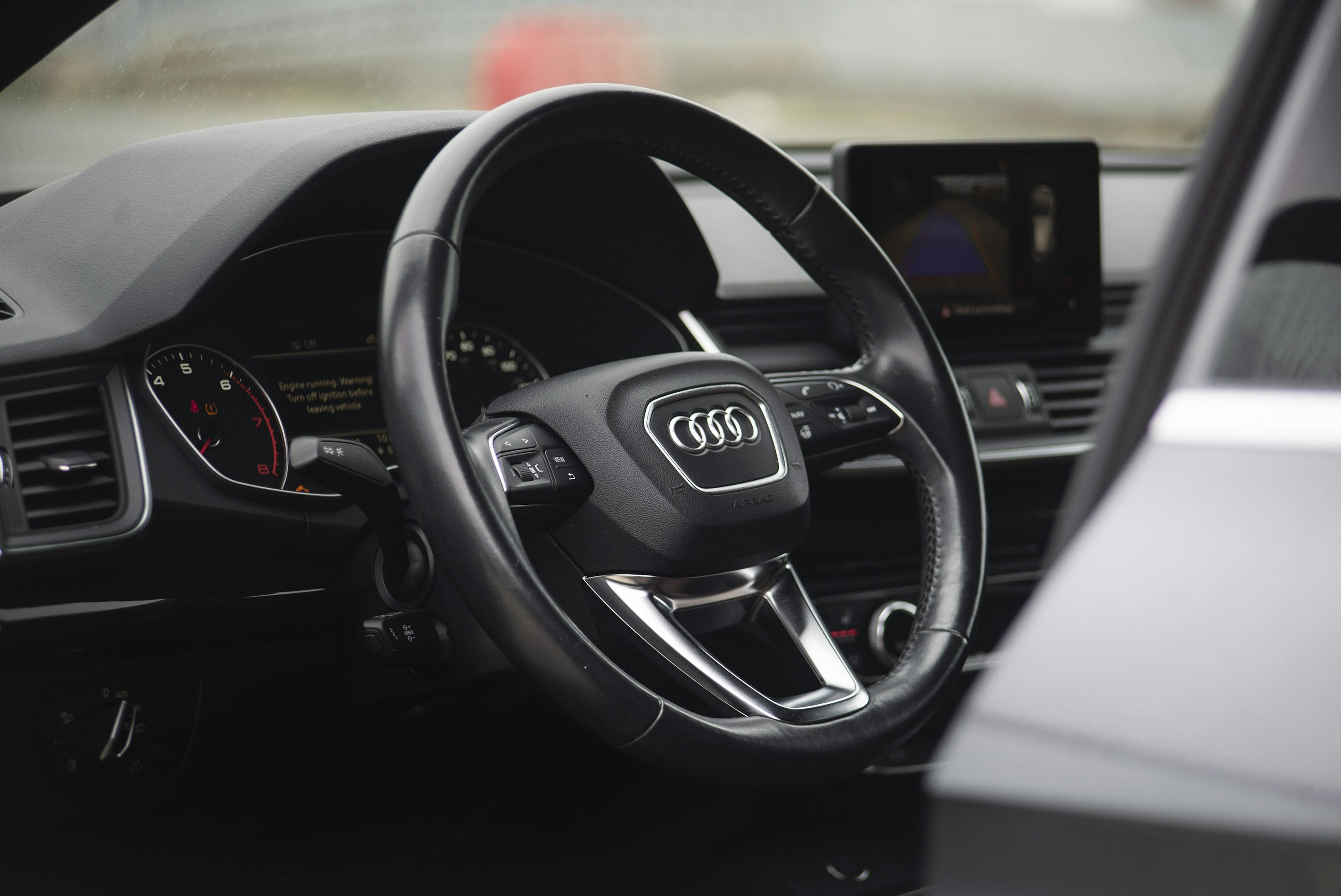 Audi cockpit with the steering wheel in the foreground and a reversing-camera view with parking guidelines on the dashboard screen.