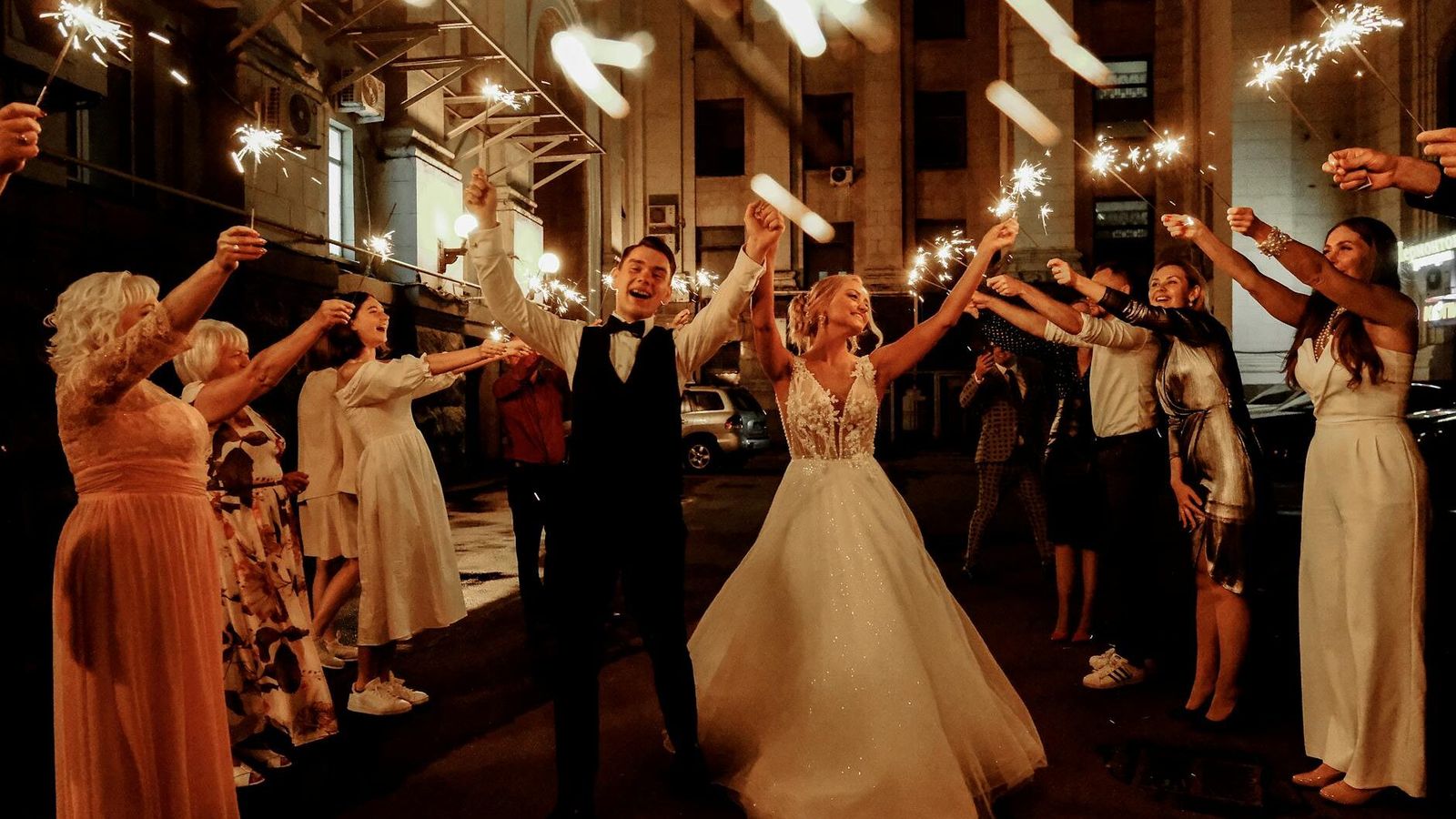 Sparkler Dance Couple dancing beneath string lights while surrounding people hold sparklers.