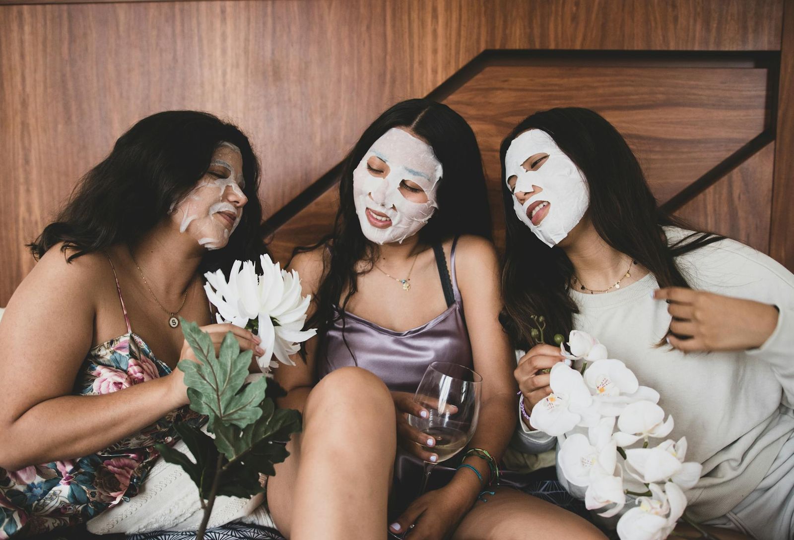 Three women sitting together with white facial masks and flowers.